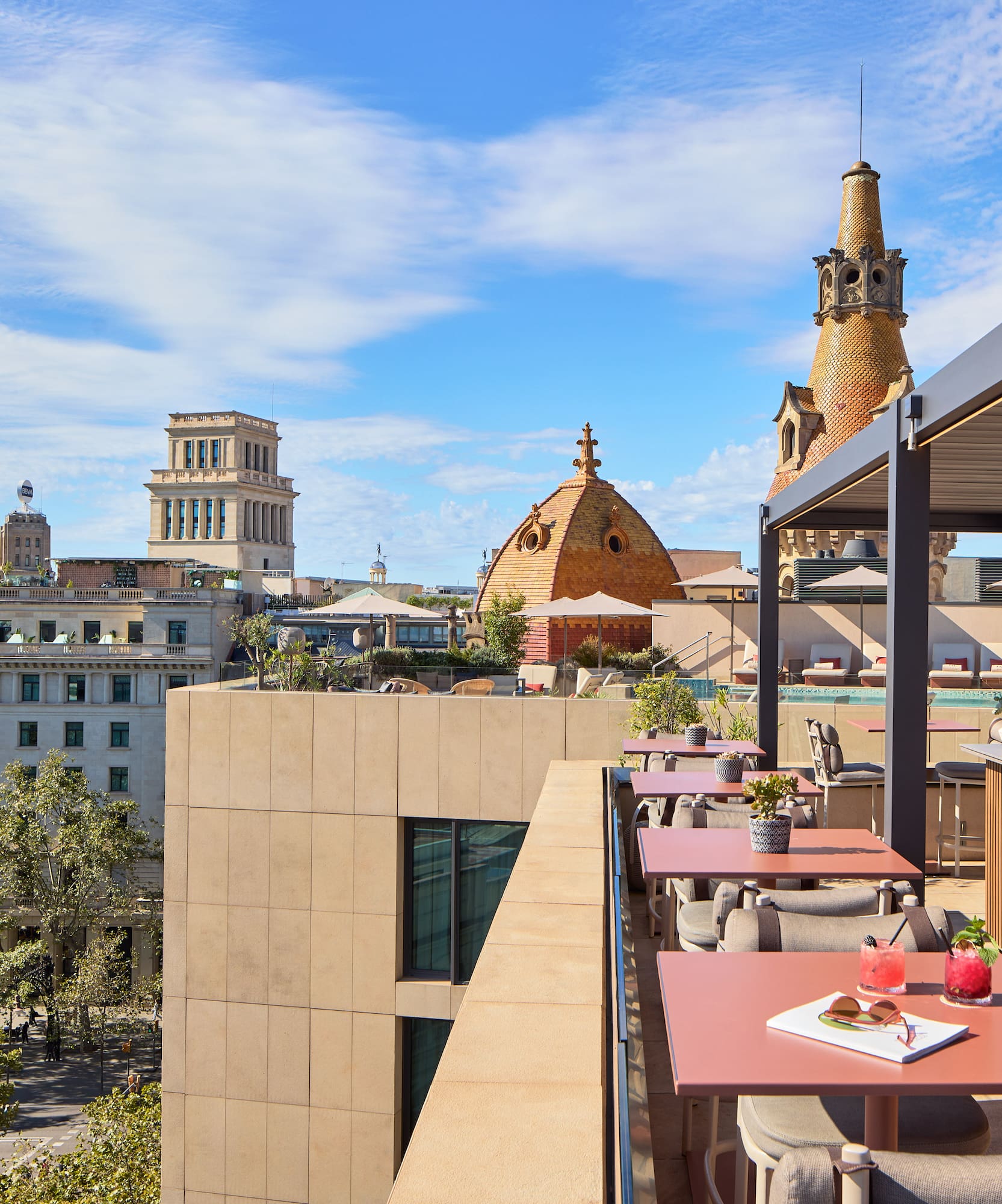 Rooftop bar terrace with cocktails, pool, and Barcelona cityscape view.
