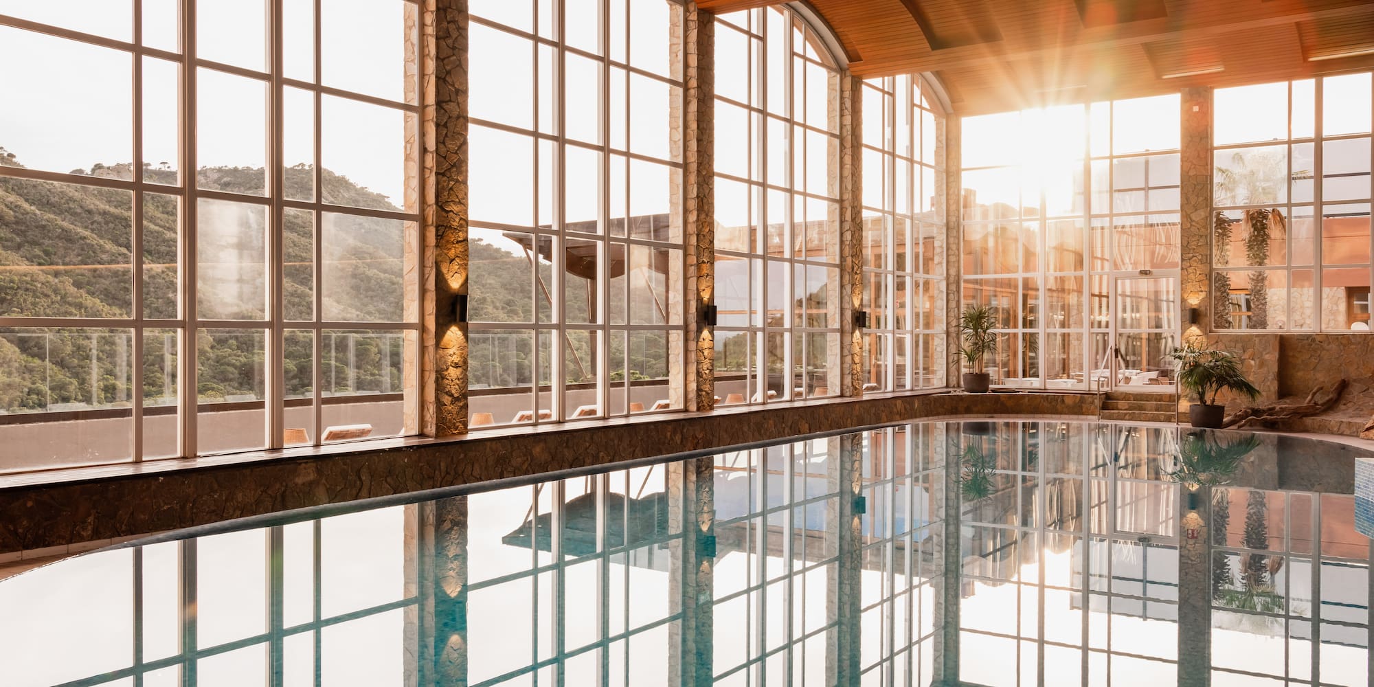 Sunlit indoor pool with panoramic mountain views and arched windows.