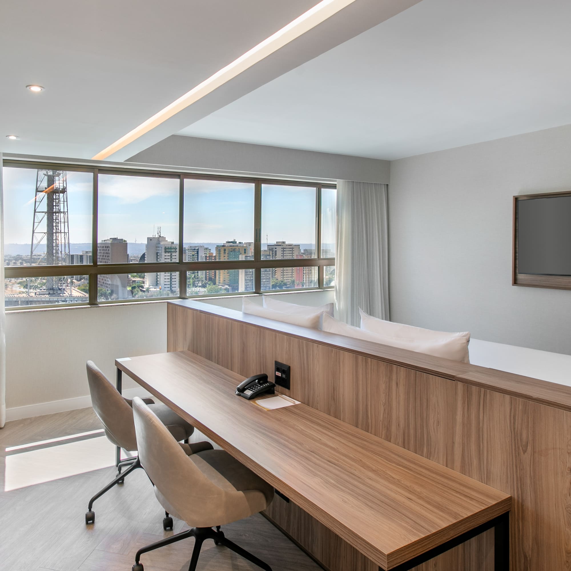 Modern hotel suite with city view, spacious desk, and wall-mounted TV.