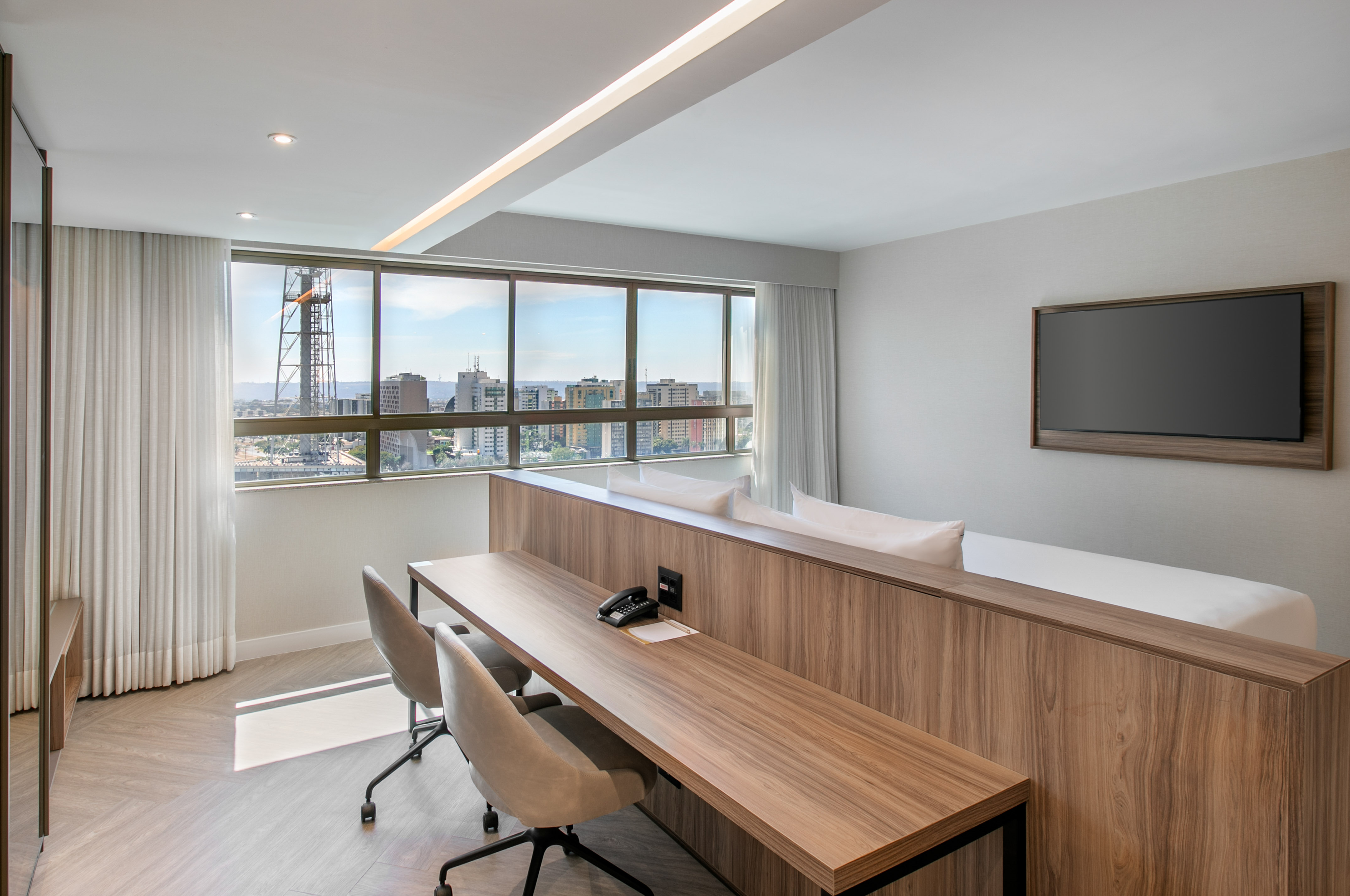 Modern hotel suite with city view, spacious desk, and wall-mounted TV.