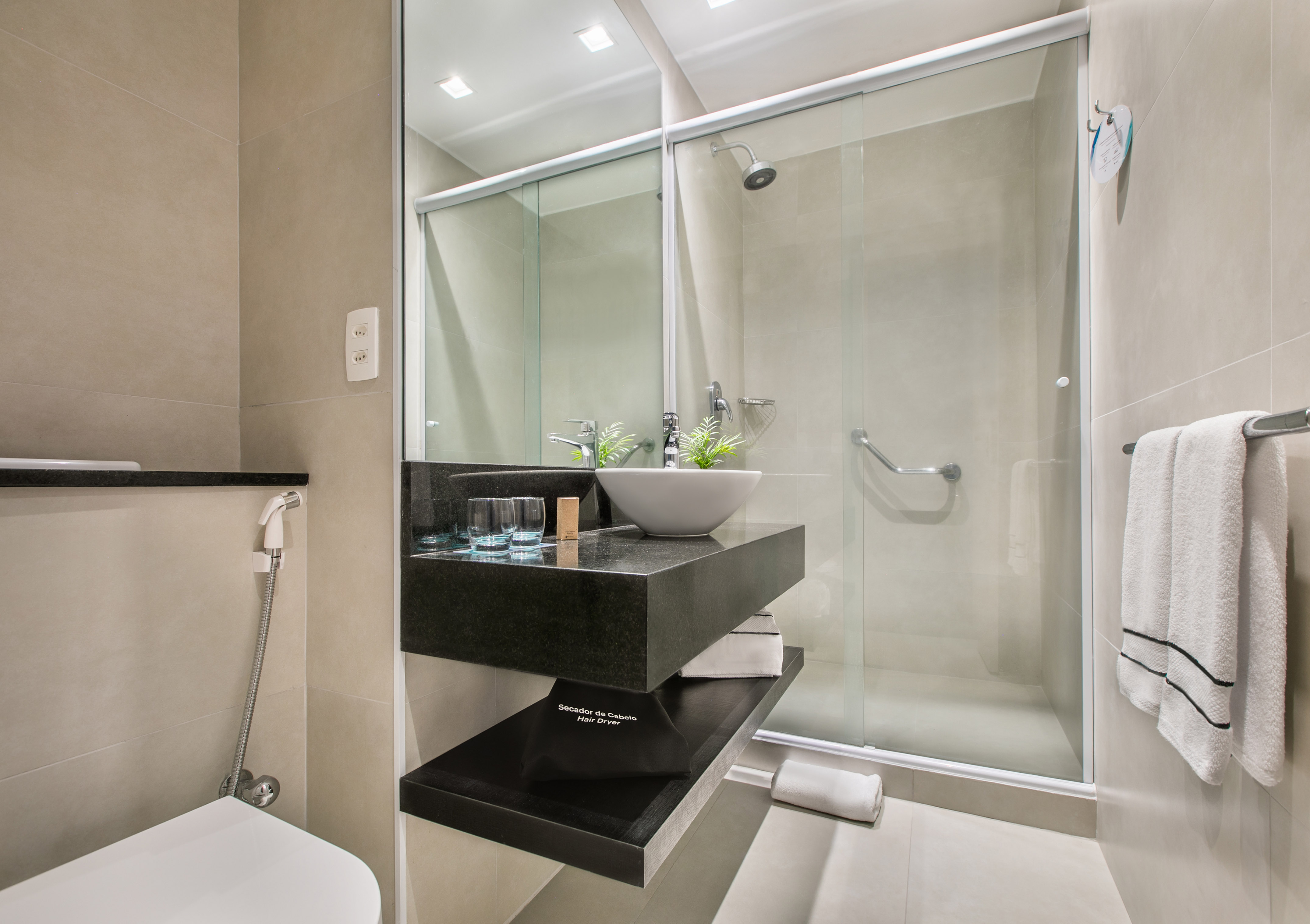 Modern hotel bathroom with floating vanity, vessel sink, glass shower, and toilet.