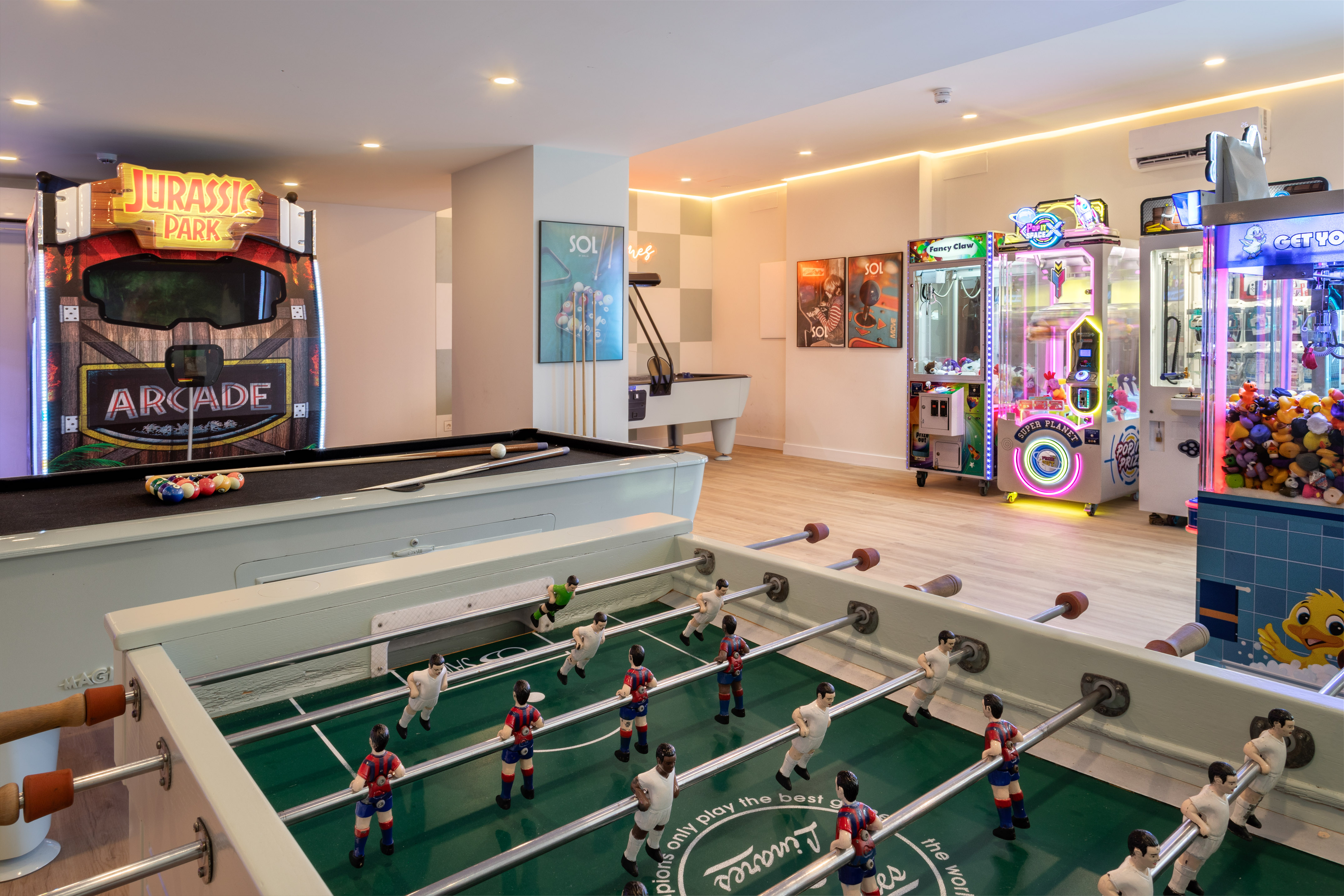 Sala de juegos con billar, futbolín y máquinas arcade populares.