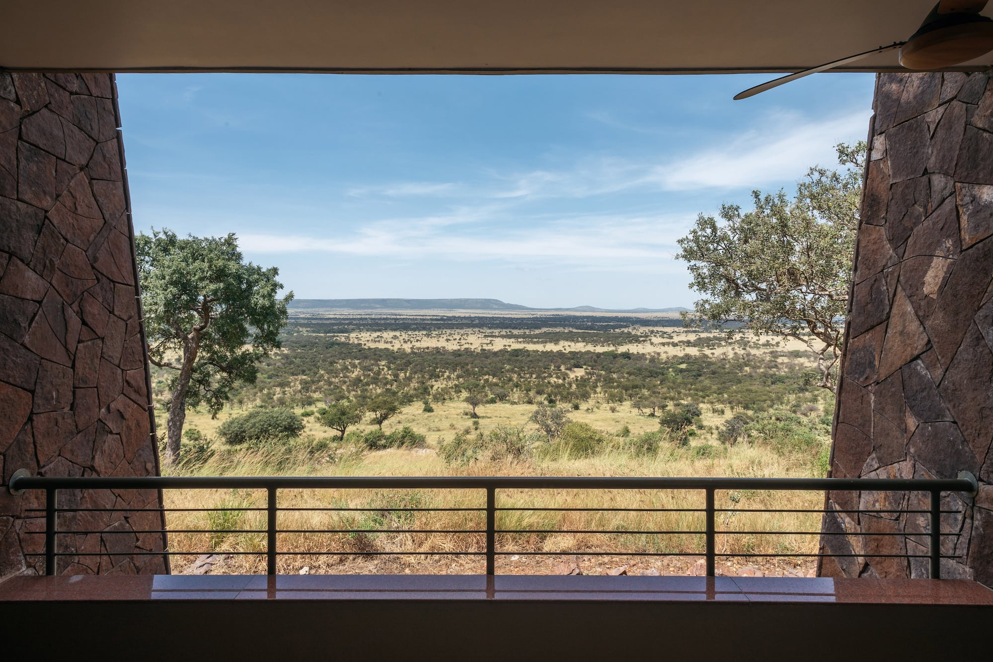 Safari lodge balcony view of vast African savanna with scattered trees and hills.