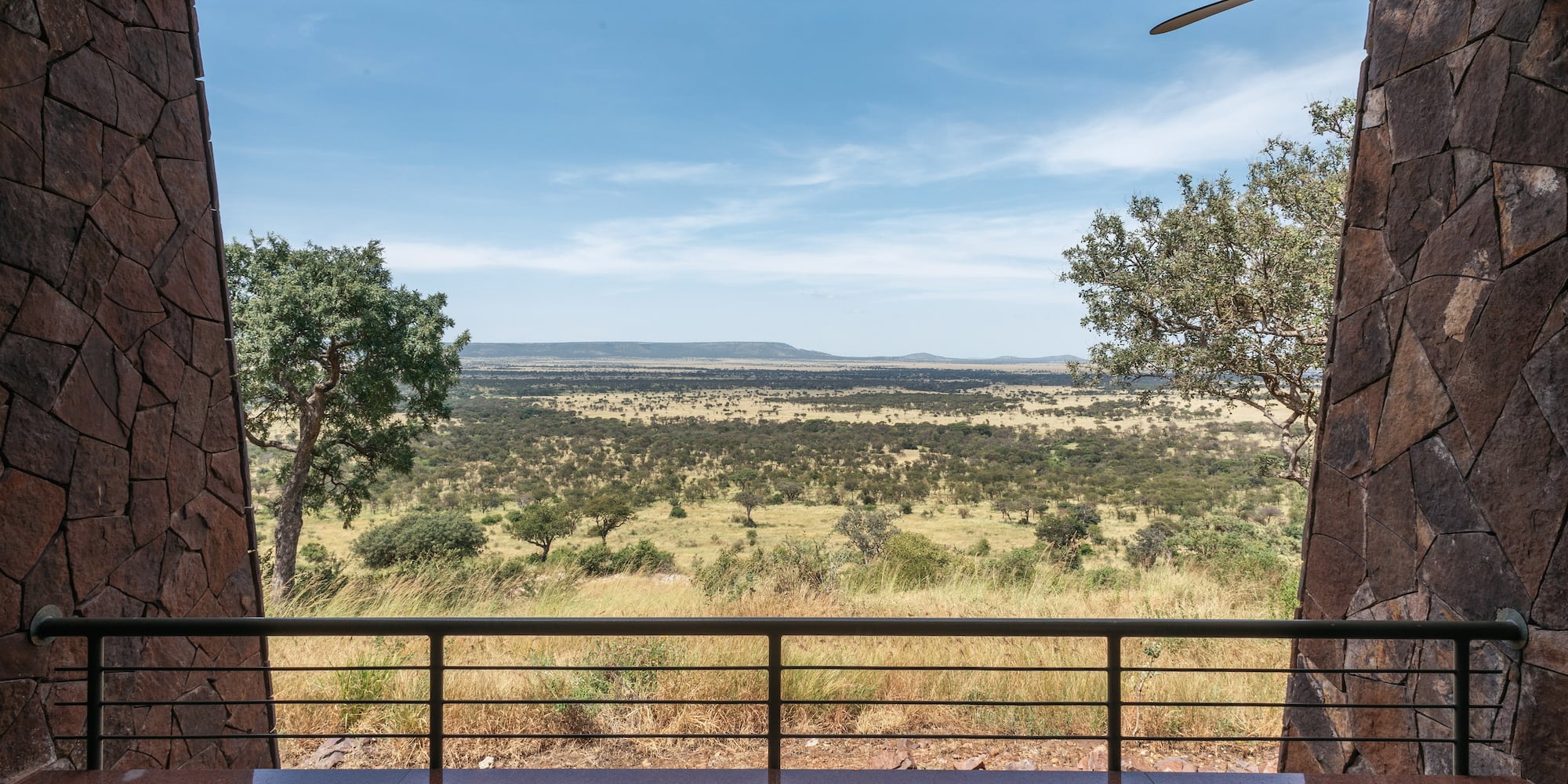 Safari lodge balcony view over sprawling African savanna, scattered trees, and hills.