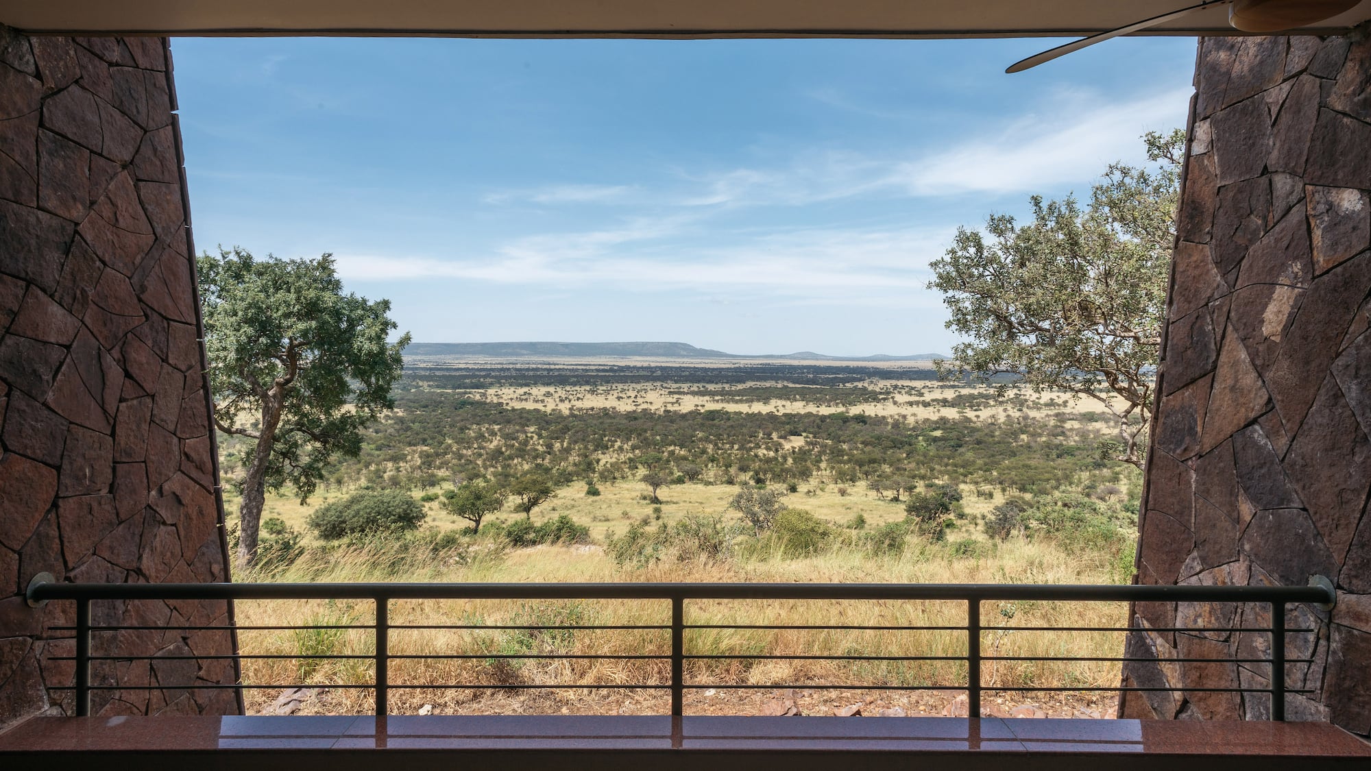 Safari lodge balcony view of vast African savanna with scattered trees and hills.