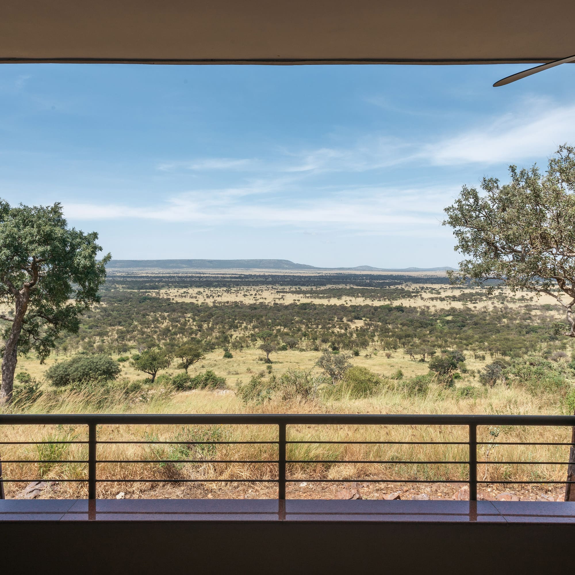 Safari lodge balcony view of vast African savanna with scattered trees and hills.