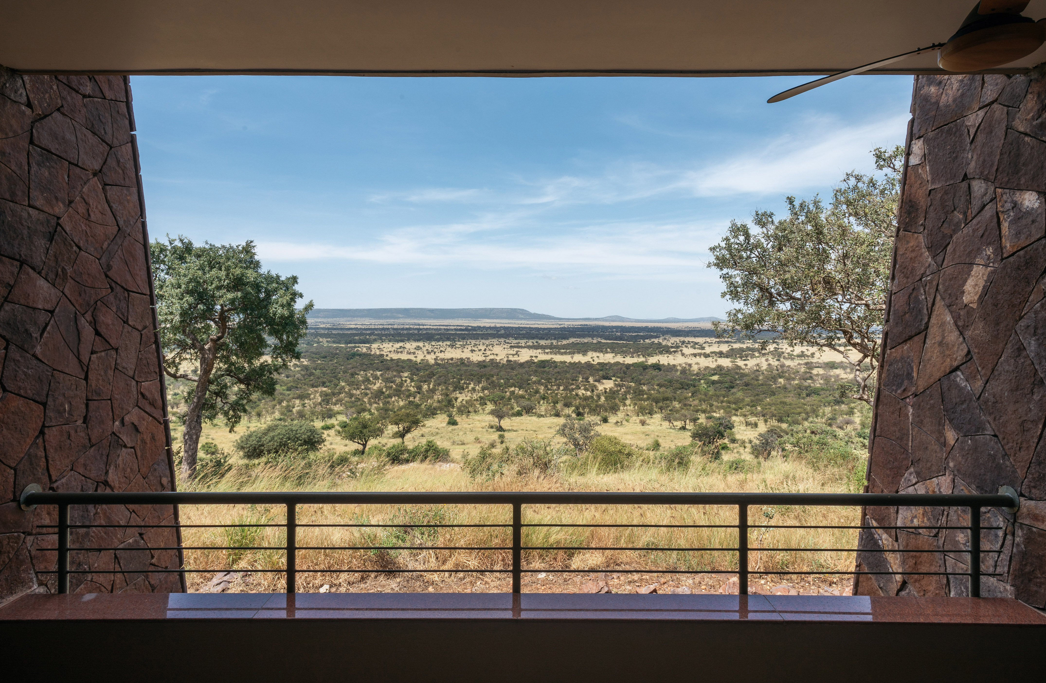 Safari lodge balcony view of vast African savanna with scattered trees and hills.