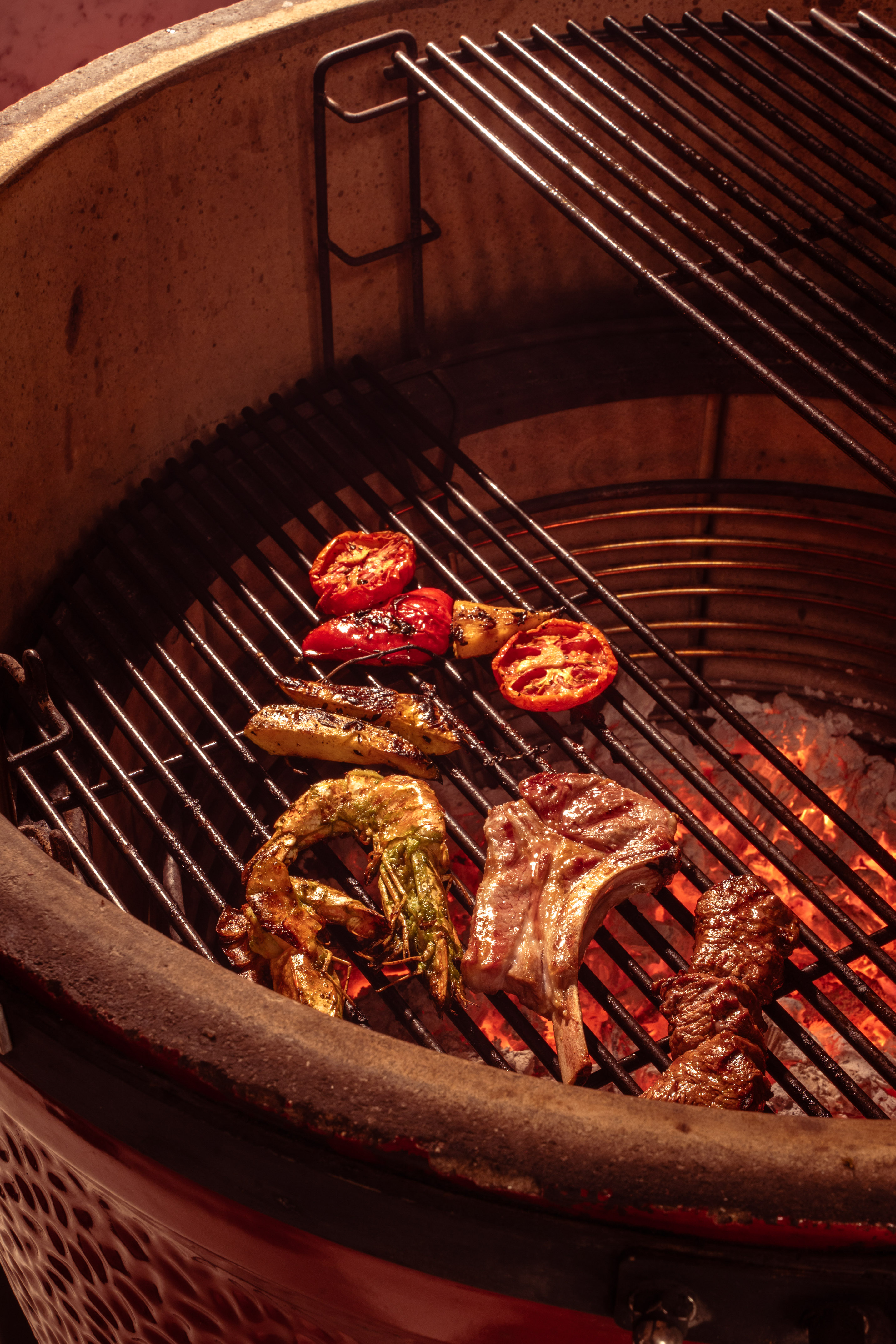 Grilling shrimp, lamb chops, tomatoes, and vegetables on a hot kamado BBQ.