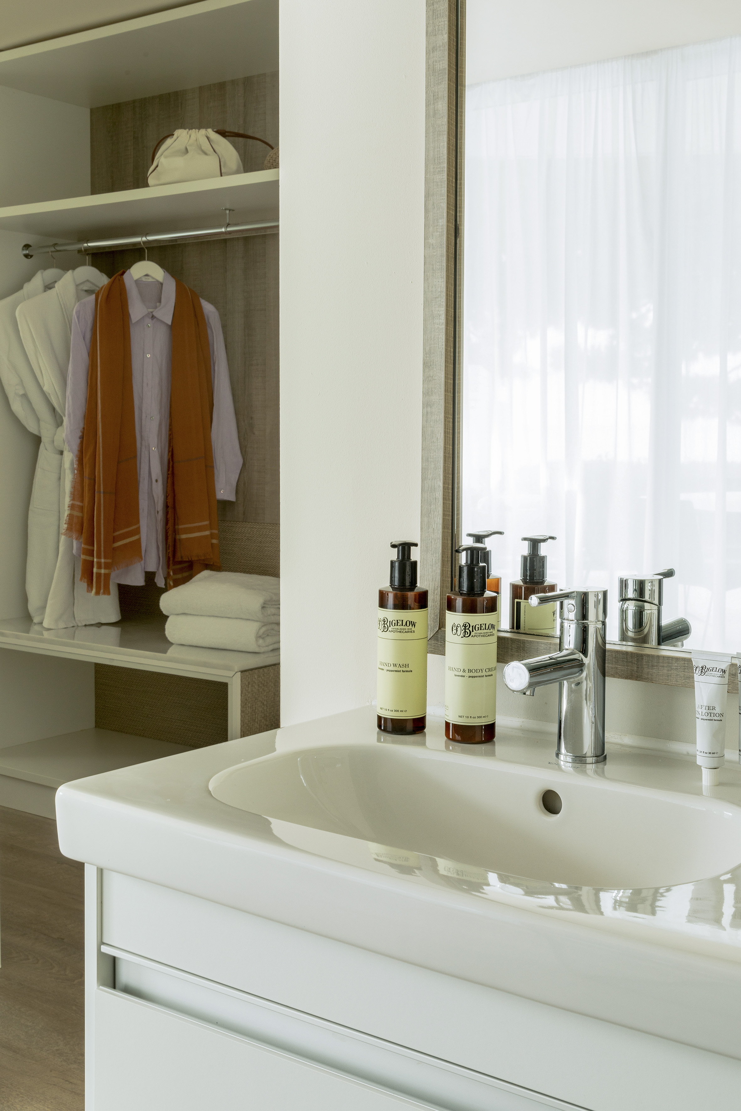 Hotel bathroom vanity with C.O. Bigelow toiletries, mirror, and open wardrobe.