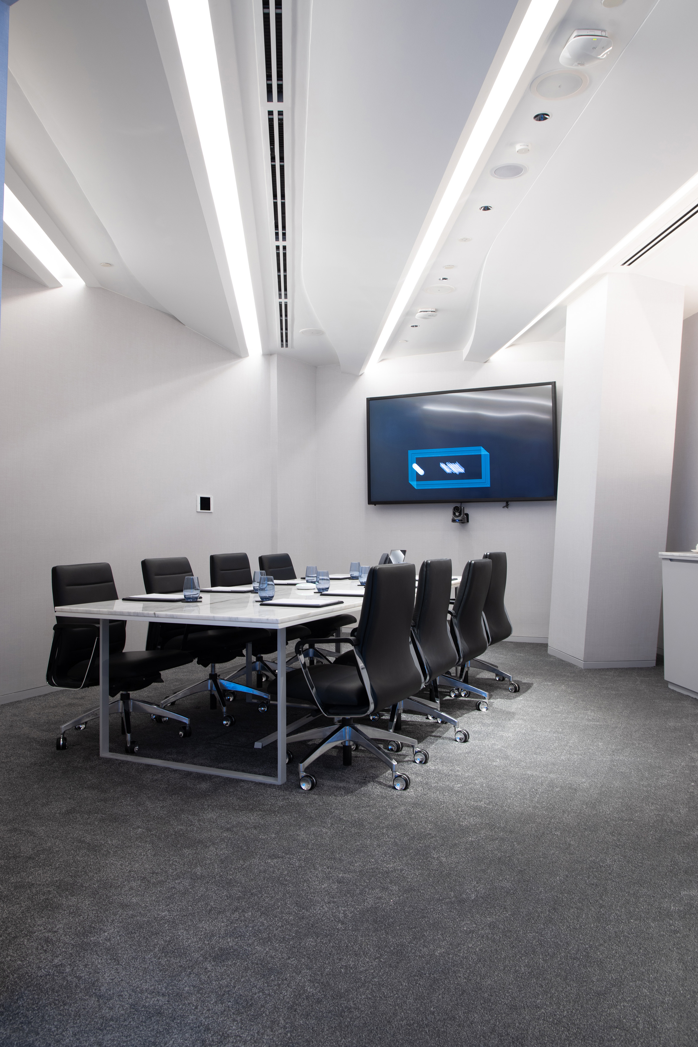 Modern conference room, white table, black chairs, large display screen.