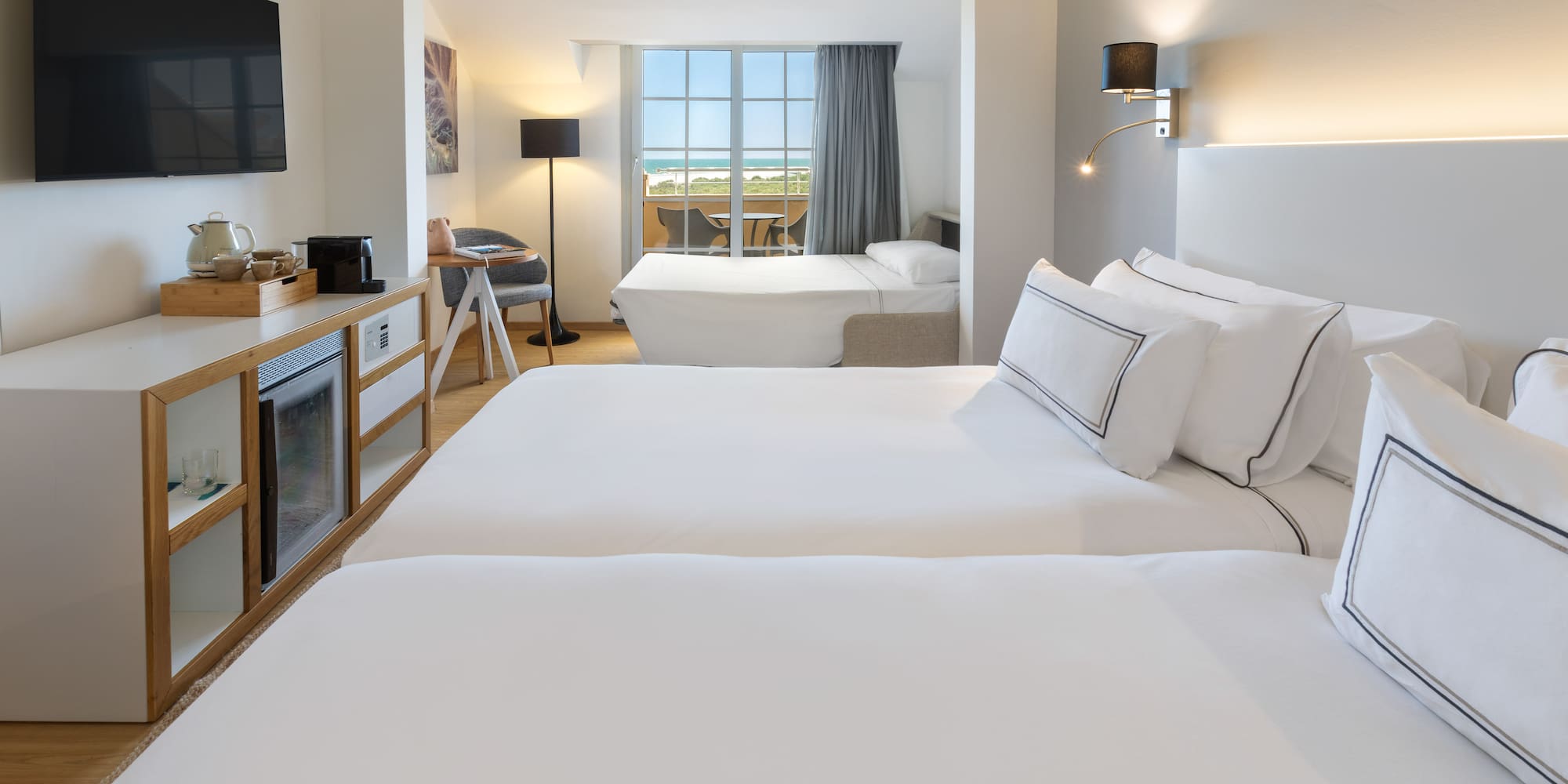 Habitación de hotel moderna con dos camas y balcón con vista al mar.