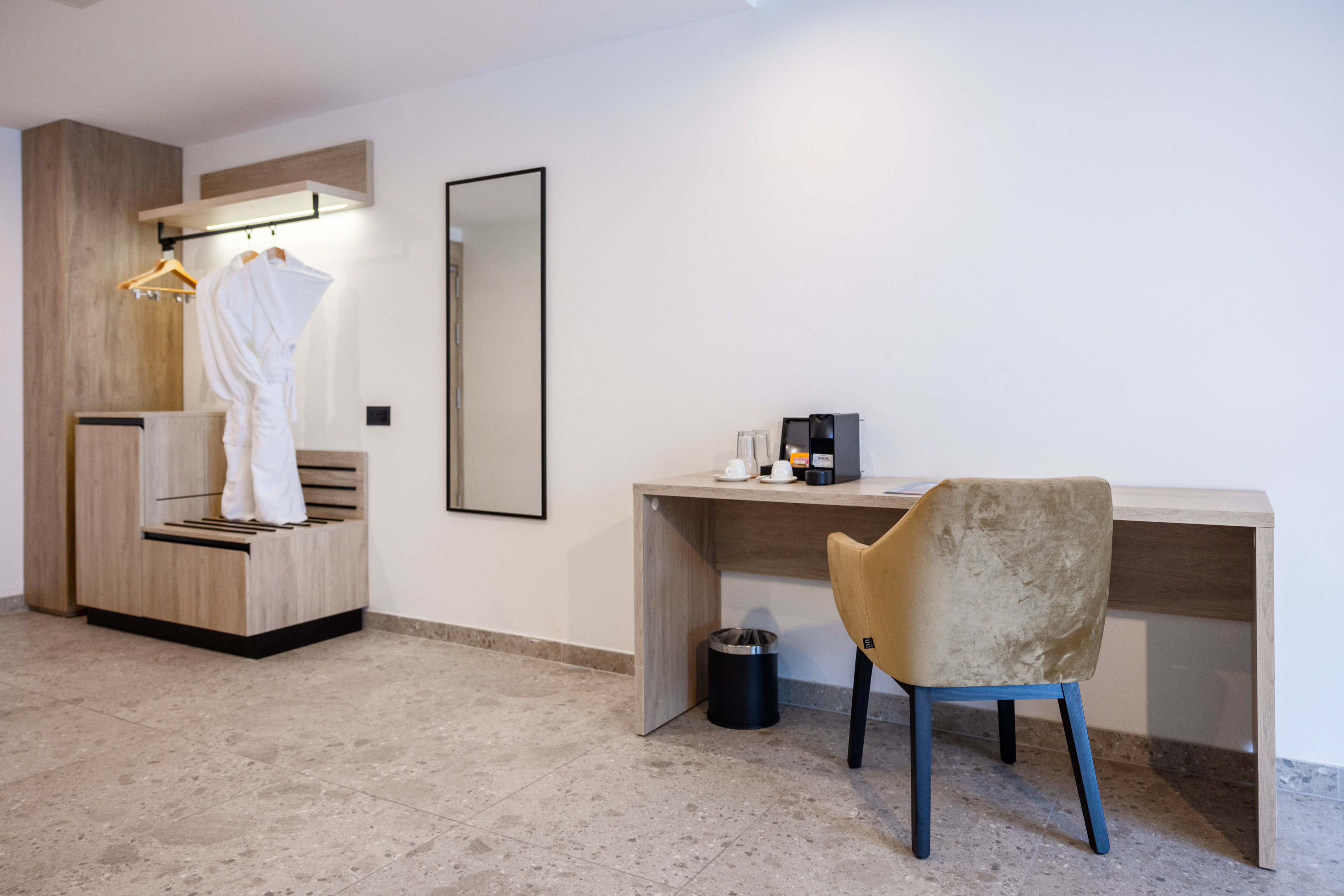 Stylish hotel room with wardrobe, white bathrobe, mirror, desk, and coffee maker.