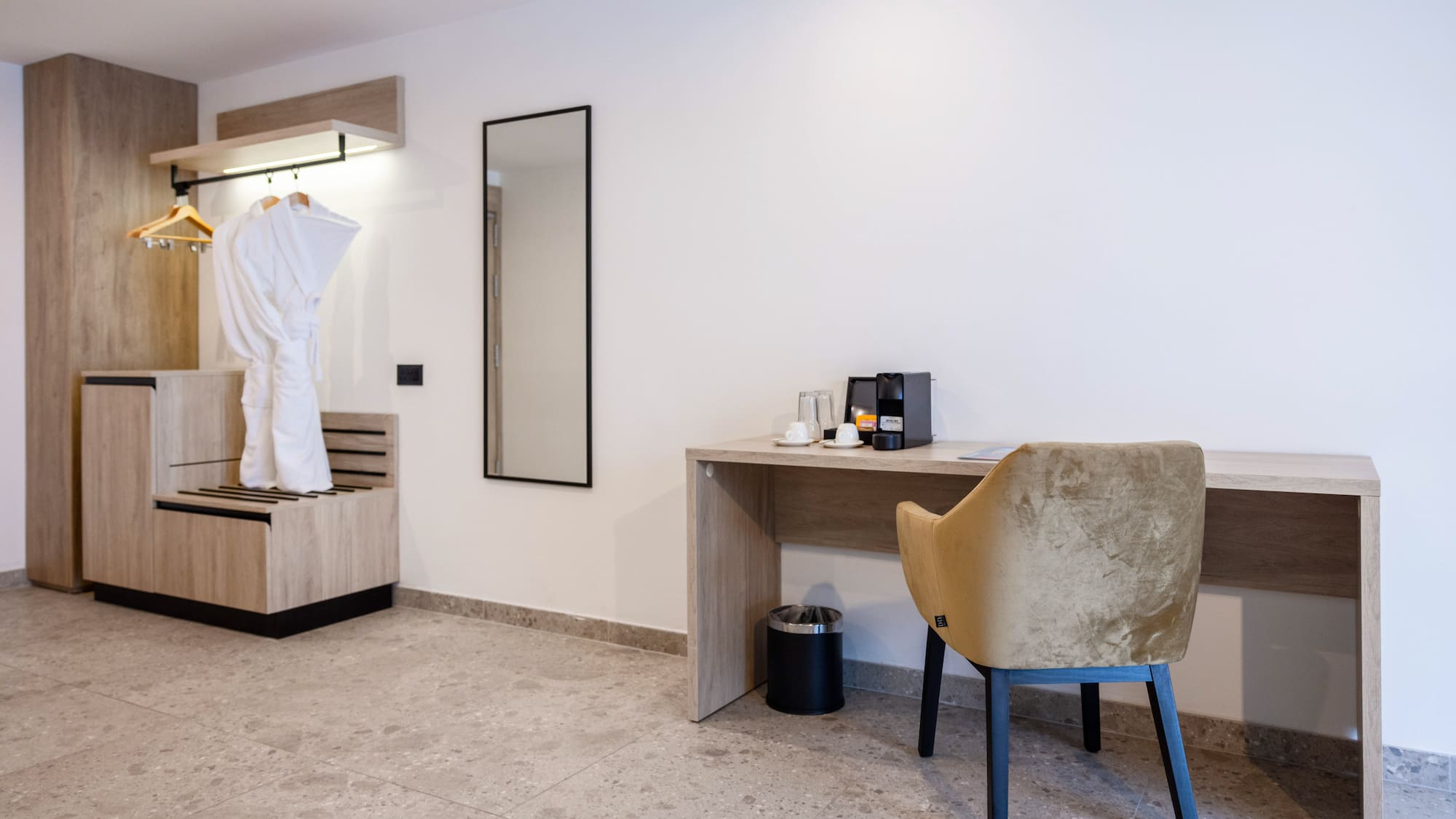 Stylish hotel room with wardrobe, white bathrobe, mirror, desk, and coffee maker.