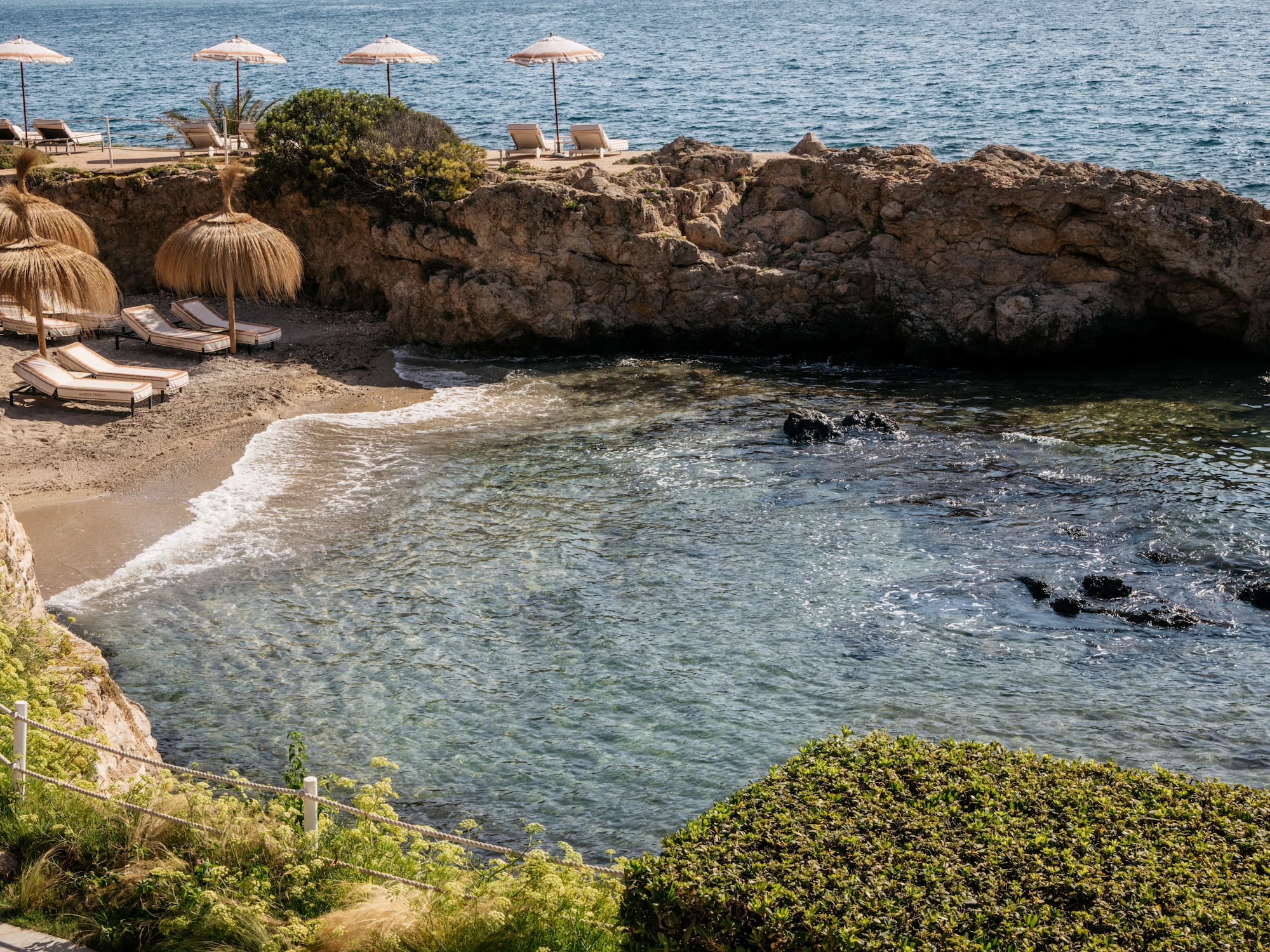 a beach with umbrellas and chairs on a rocky shore