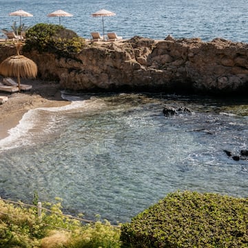 a beach with umbrellas and chairs on a rocky shore.