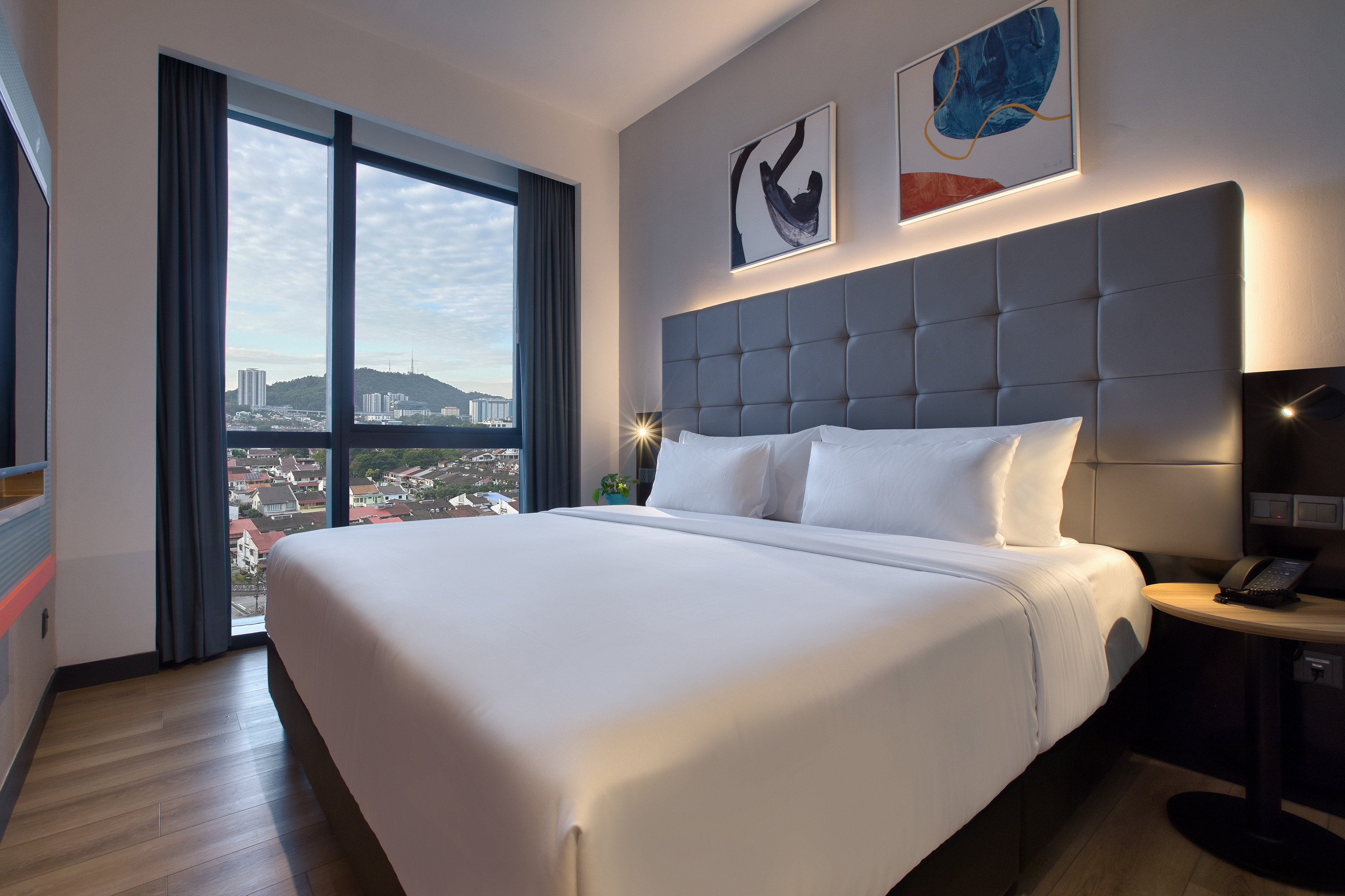 Modern hotel bedroom with a large bed, city view from window, and sleek design.