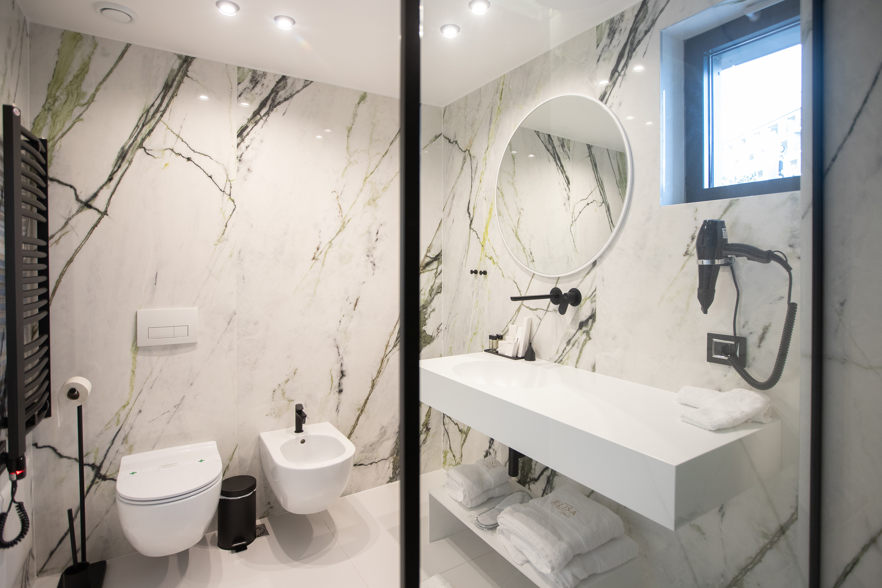 Modern marble bathroom with white vanity, toilet, bidet, and black fixtures.