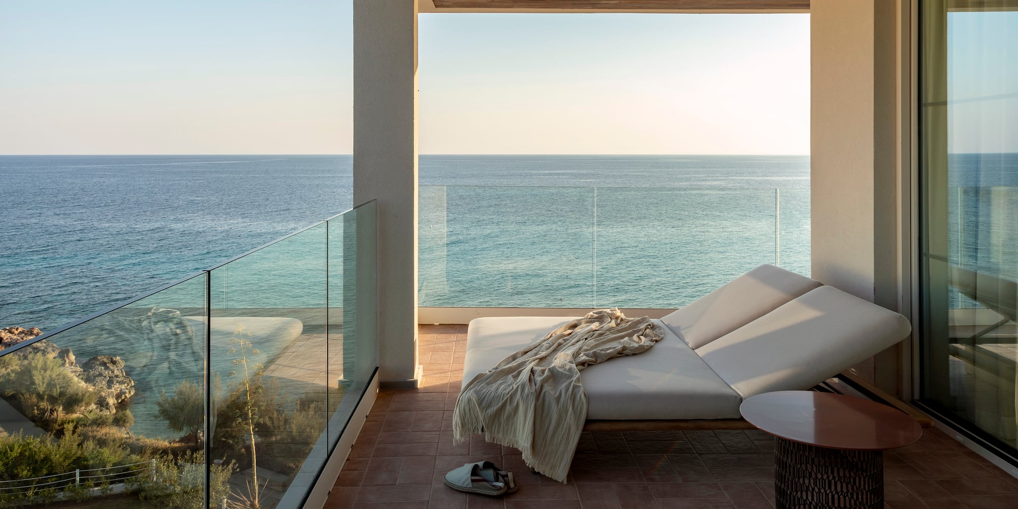 a deck with a chair and a table and a glass railing overlooking the ocean