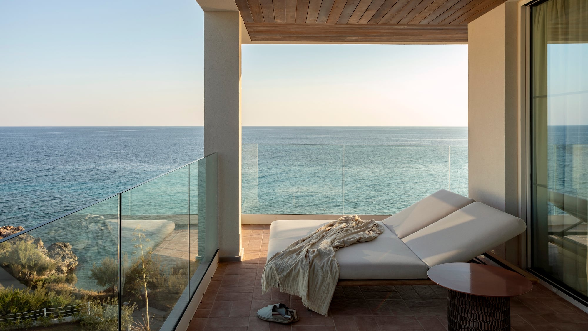a deck with a chair and a table and a glass railing overlooking the ocean