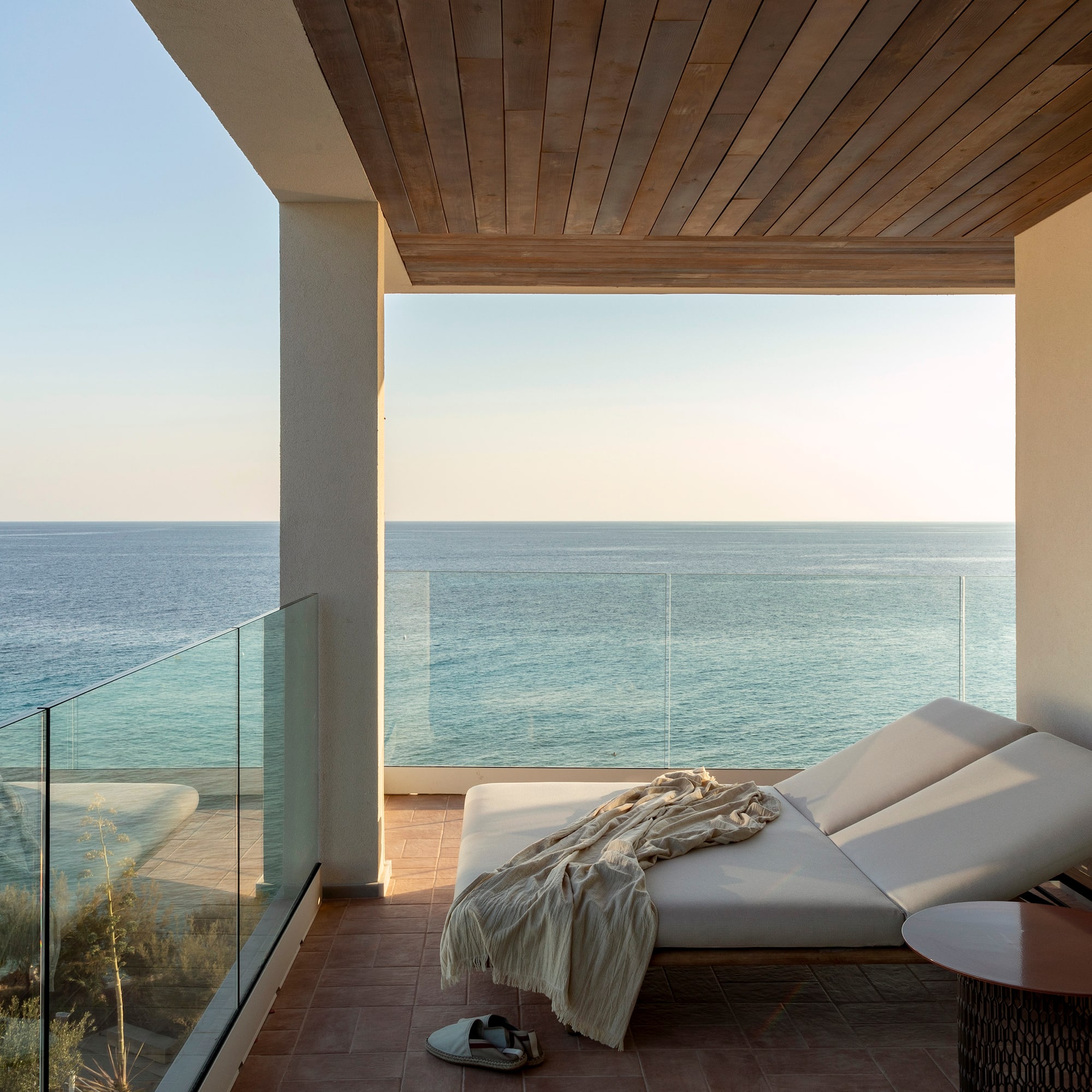 a deck with a chair and a table and a glass railing overlooking the ocean