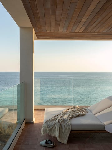 a deck with a chair and a table and a glass railing overlooking the ocean