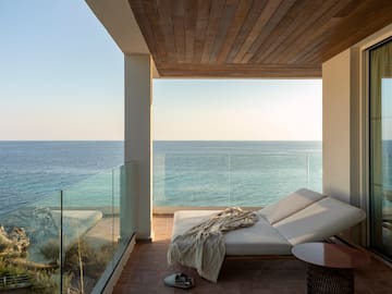 a deck with a chair and a table and a glass railing overlooking the ocean