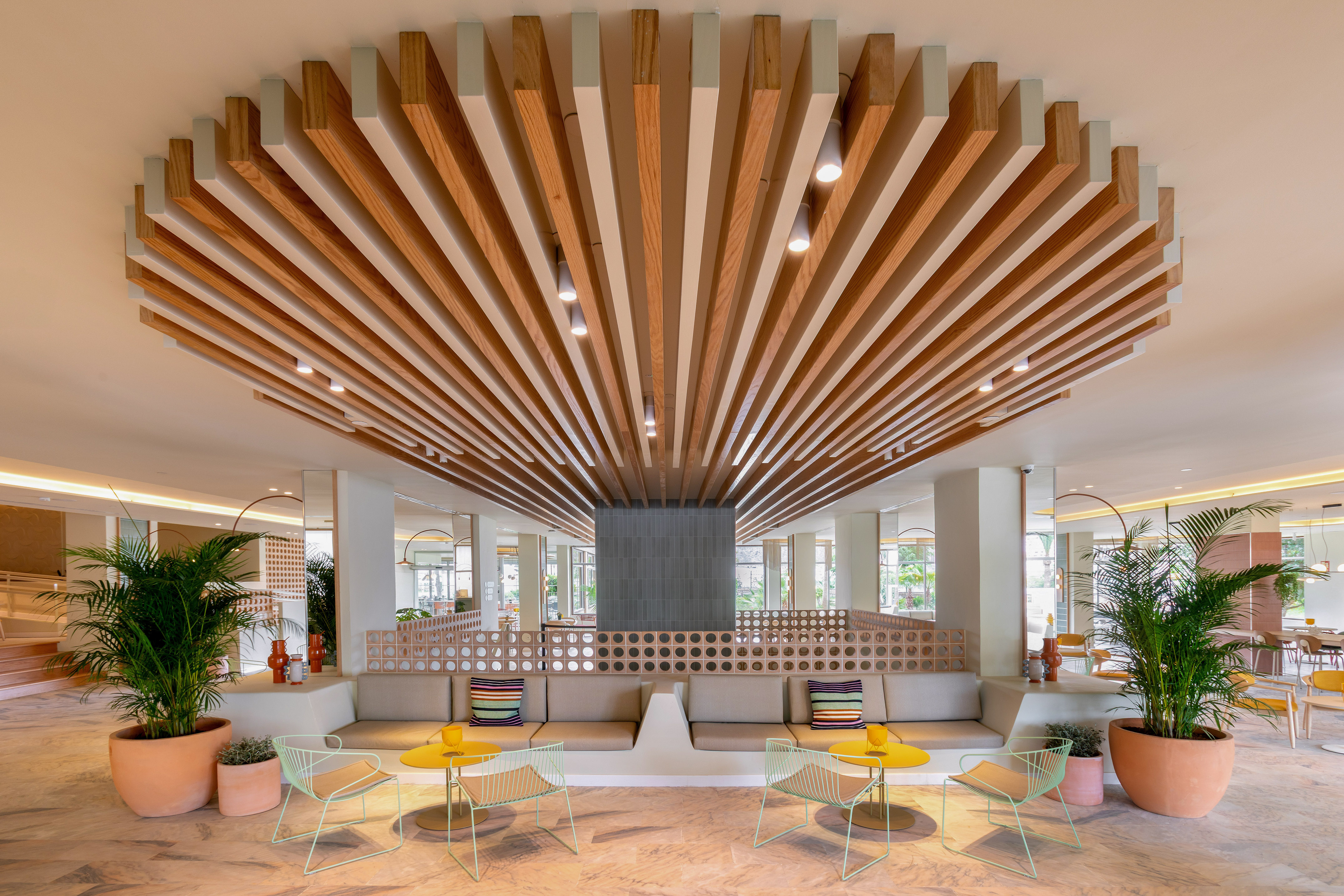 Modern lounge with fanned wooden slat ceiling, comfortable seating, and green plants.