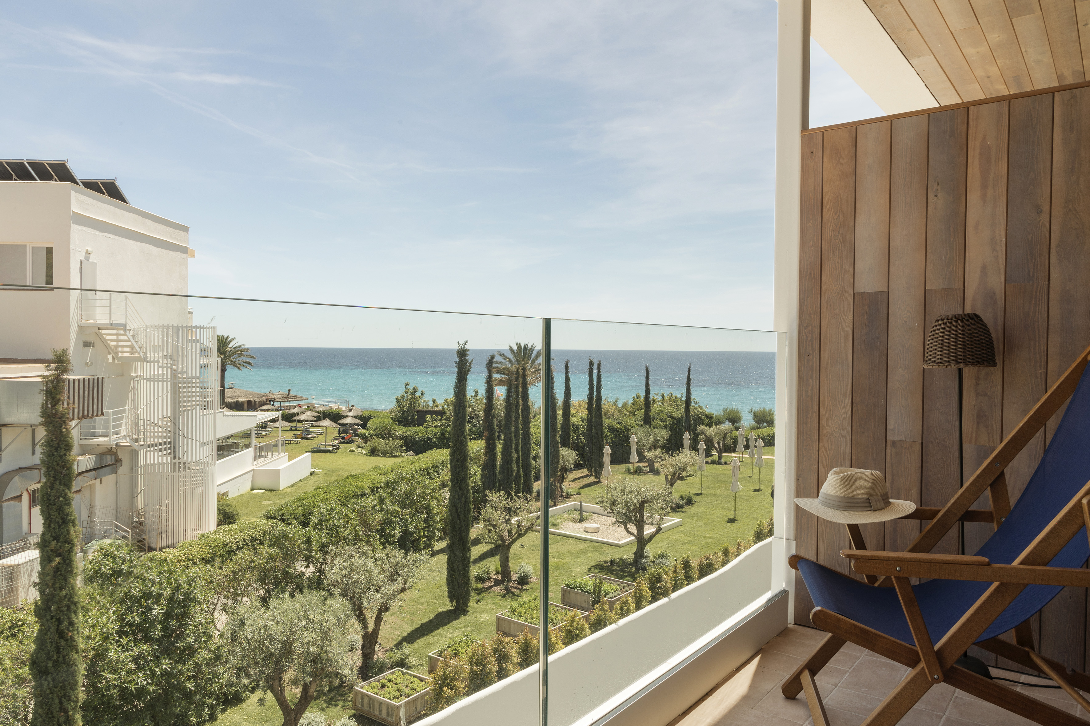 Balcony overlooking turquoise sea, hotel gardens, and beach resort.