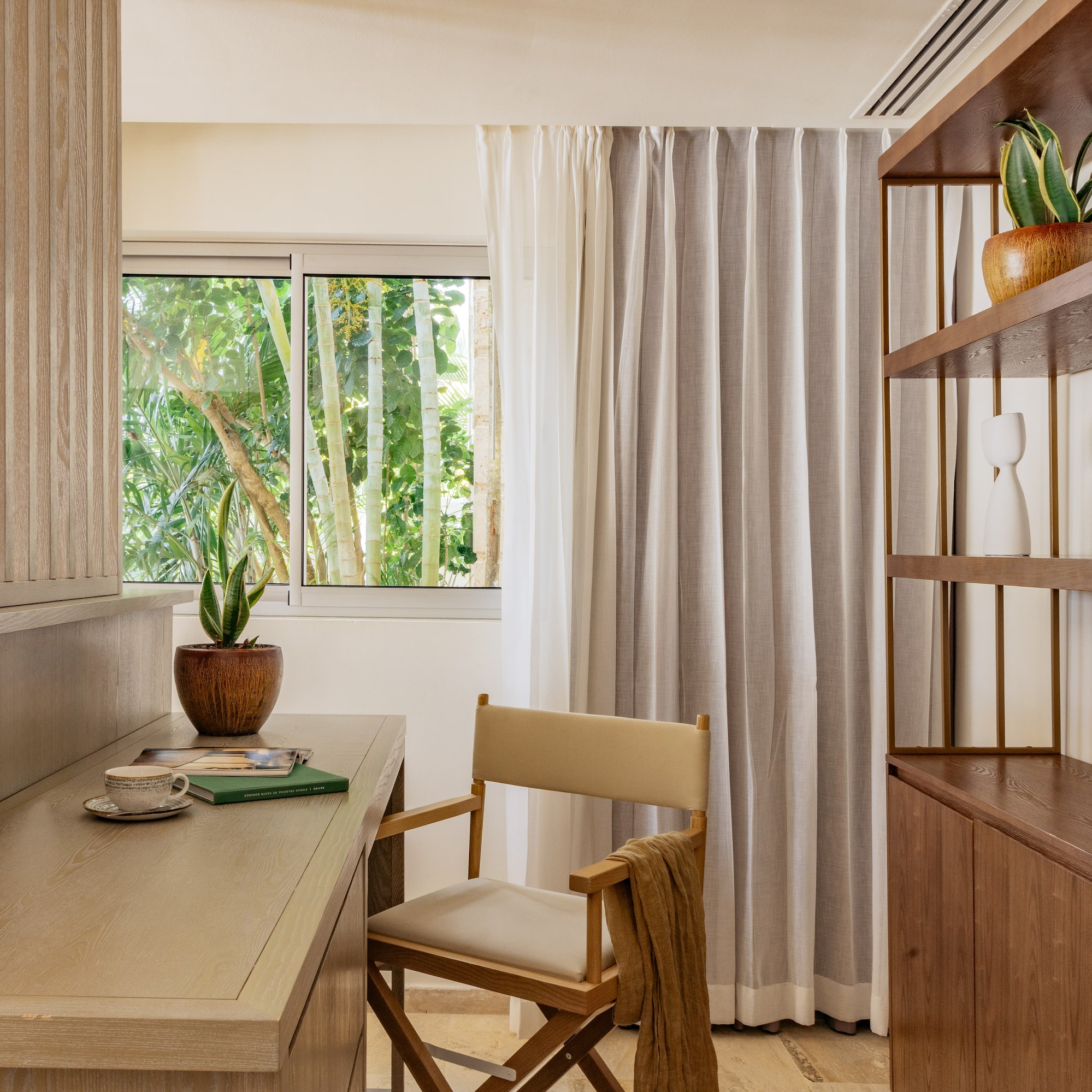 Modern wood desk with director's chair, tropical window view, and bookshelf.