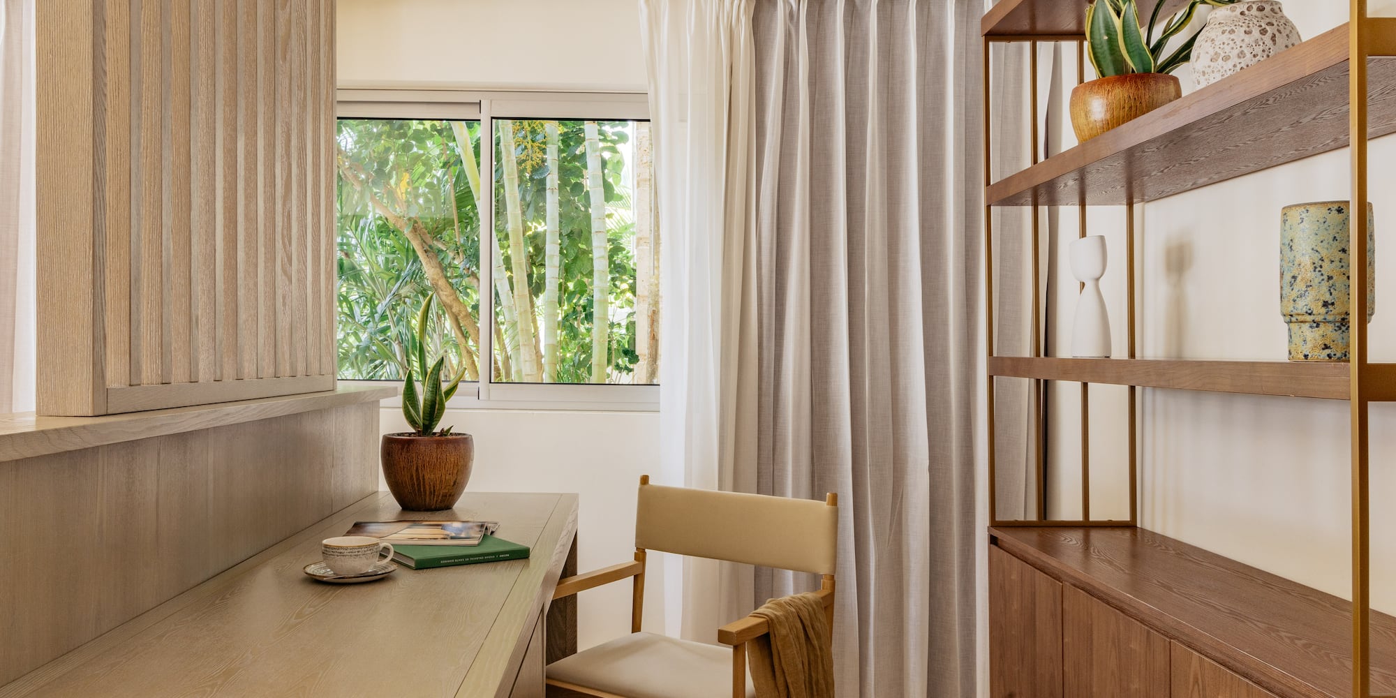 Modern wood desk with director's chair, tropical window view, and bookshelf.