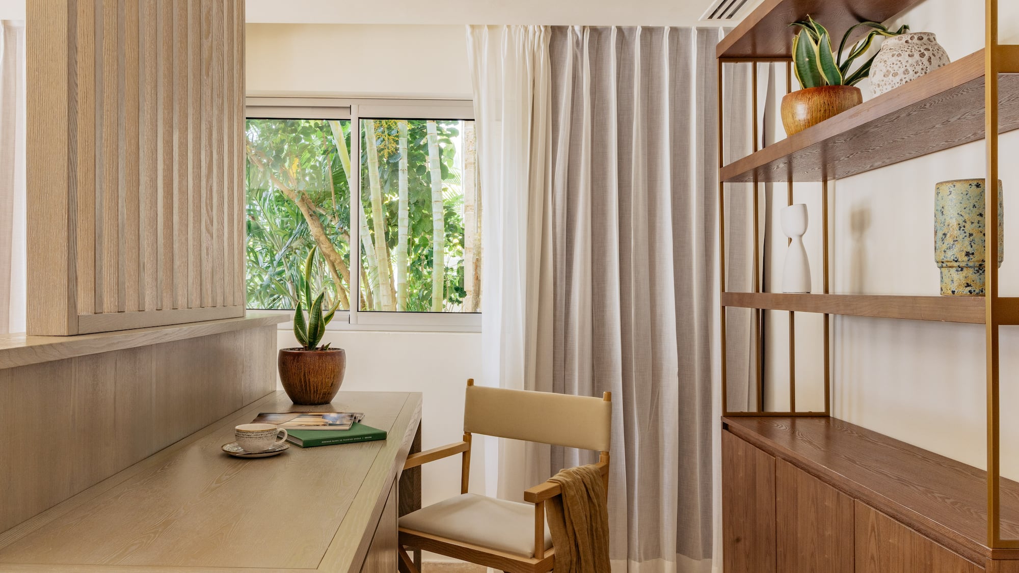 Modern wood desk with director's chair, tropical window view, and bookshelf.