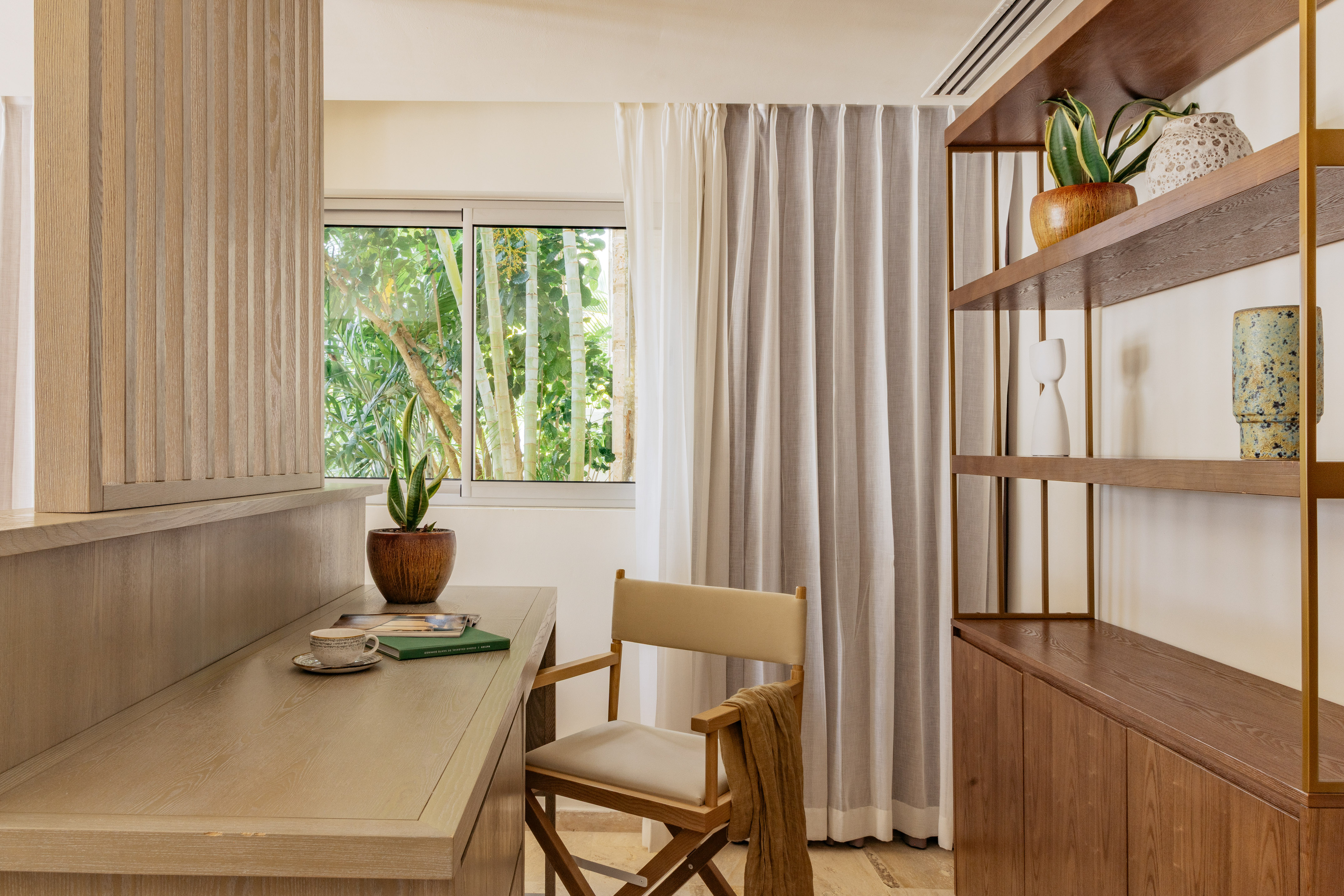 Modern wood desk with director's chair, tropical window view, and bookshelf.