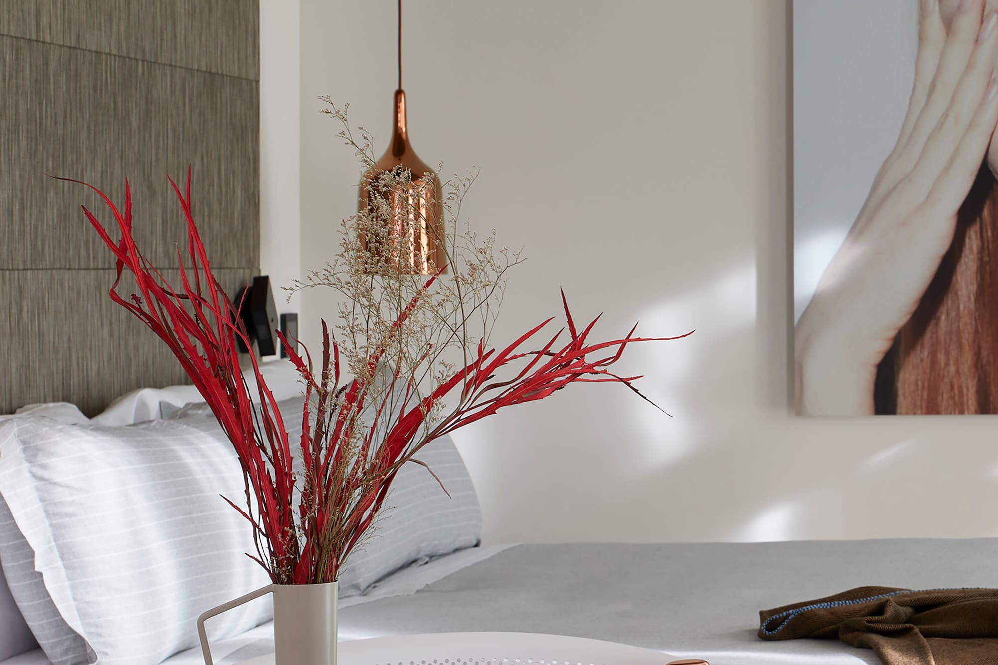 a vase of red branches on a table next to a bed