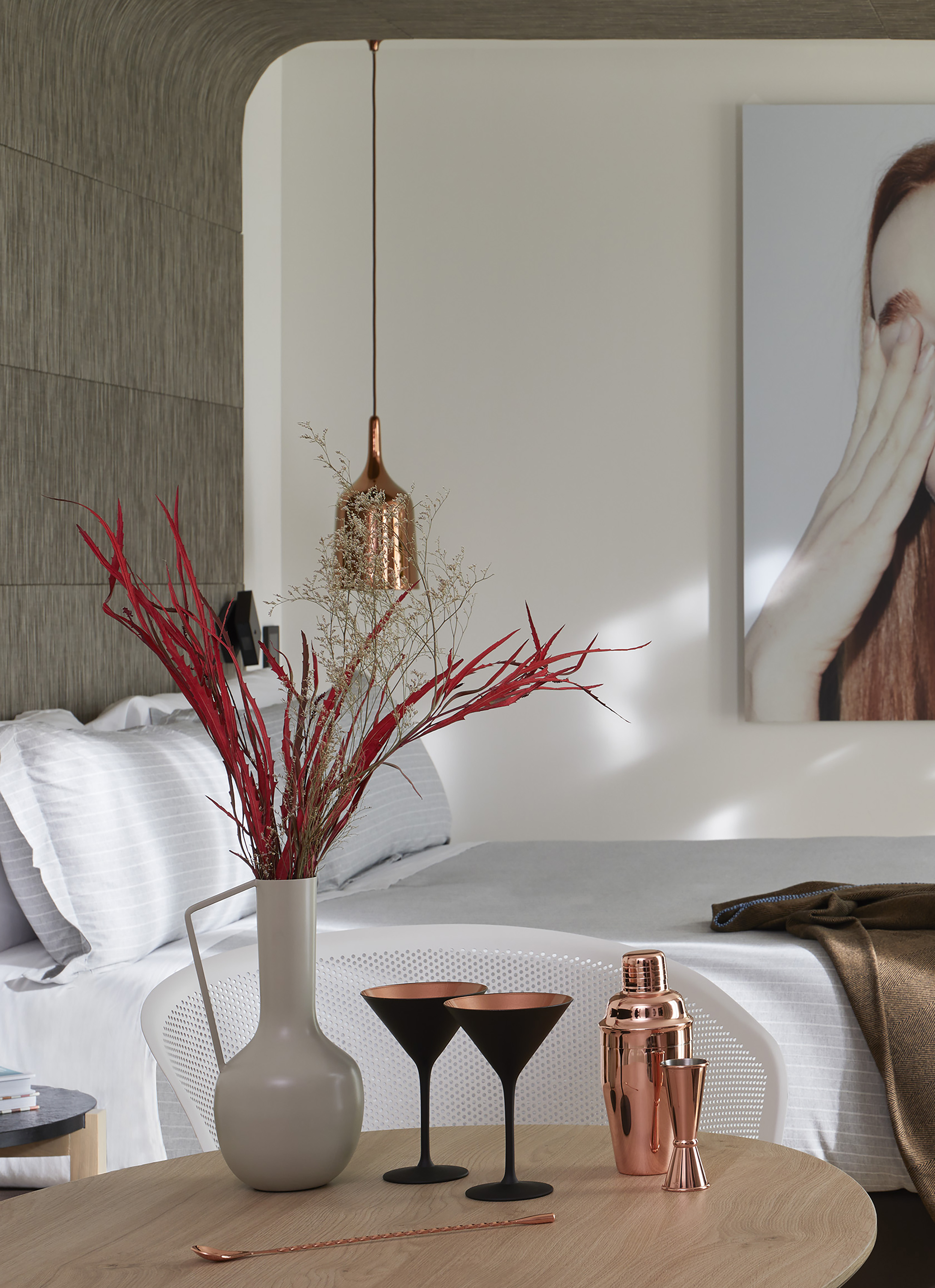 a vase of red branches on a table next to a bed