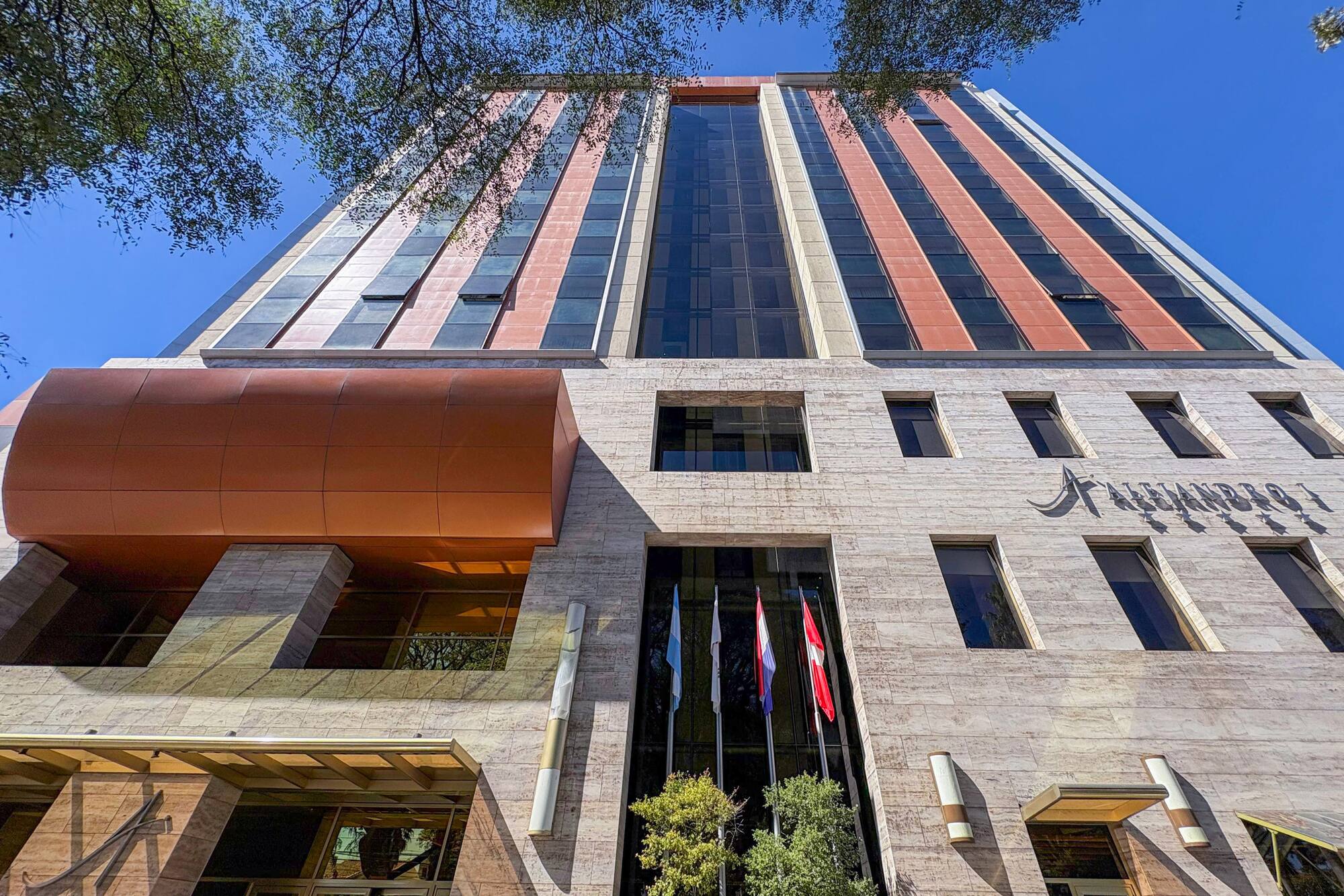 Alejandro I Hotel, modern facade with glass, stone, and flags.