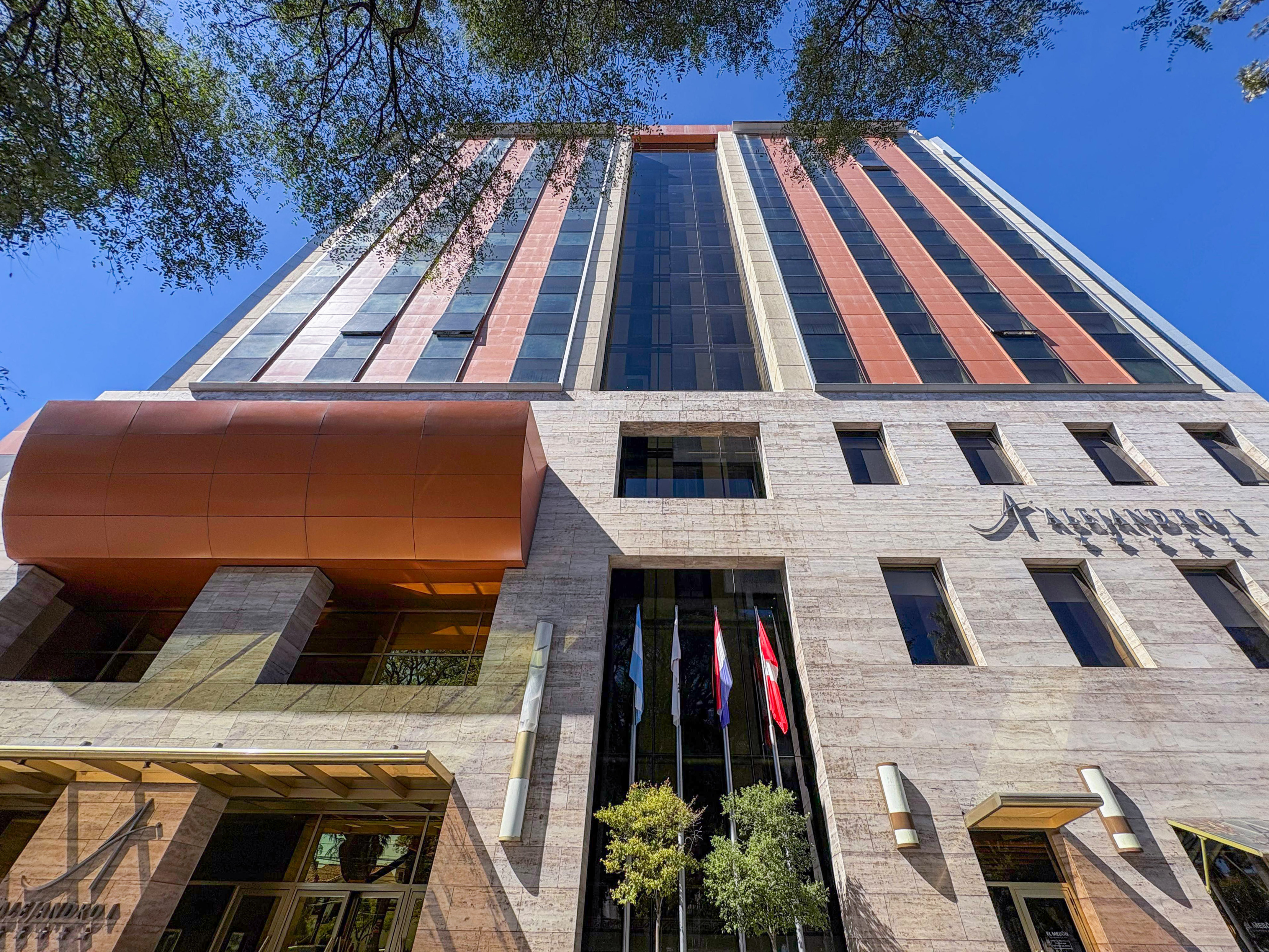 Alejandro I Hotel, modern facade with glass, stone, and flags.