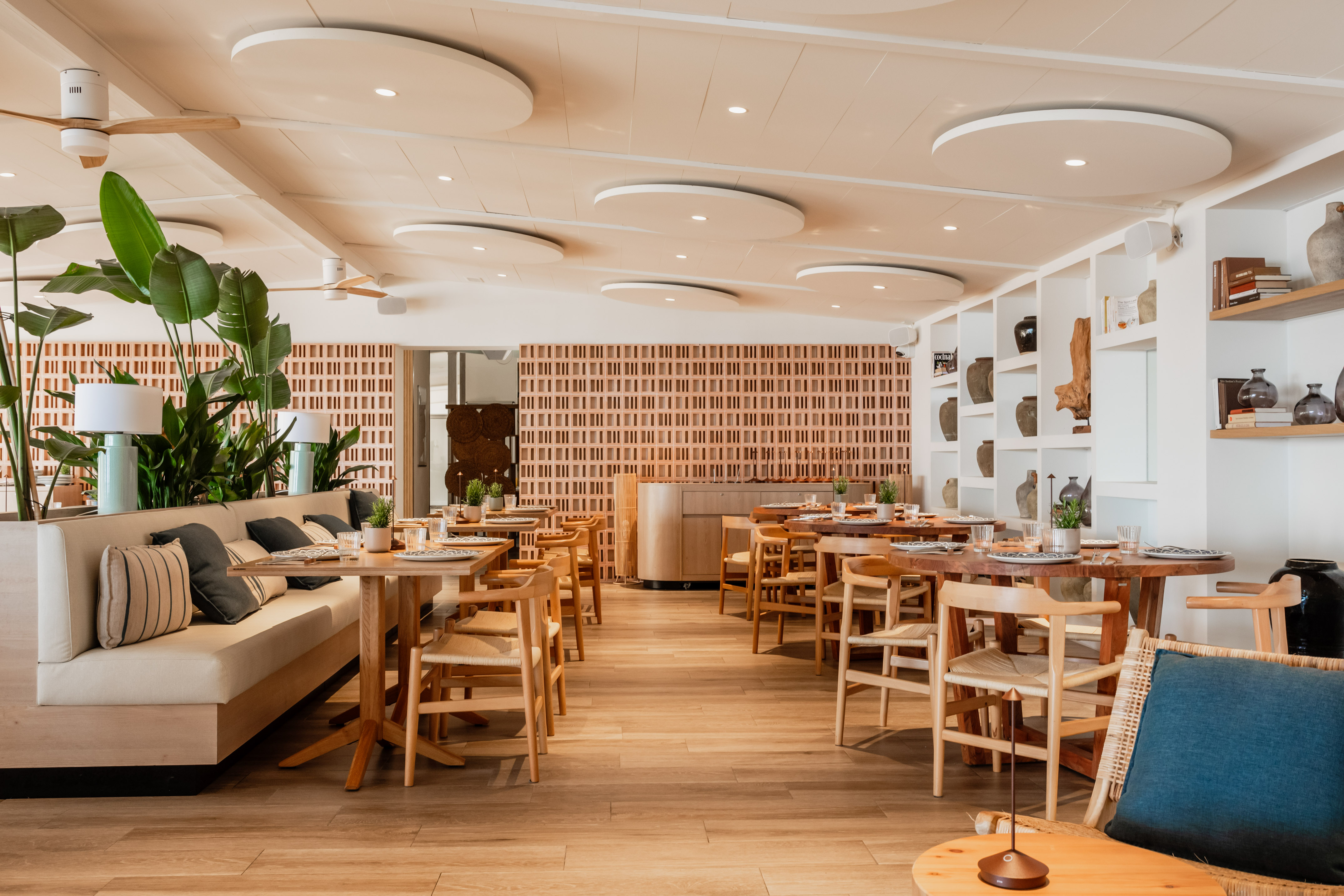 Bright modern dining room with wood tables, banquette seating, and tropical plants.
