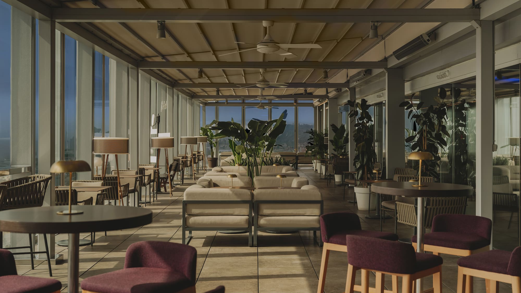 Modern covered terrace lounge with varied seating, plants, and large windows.
