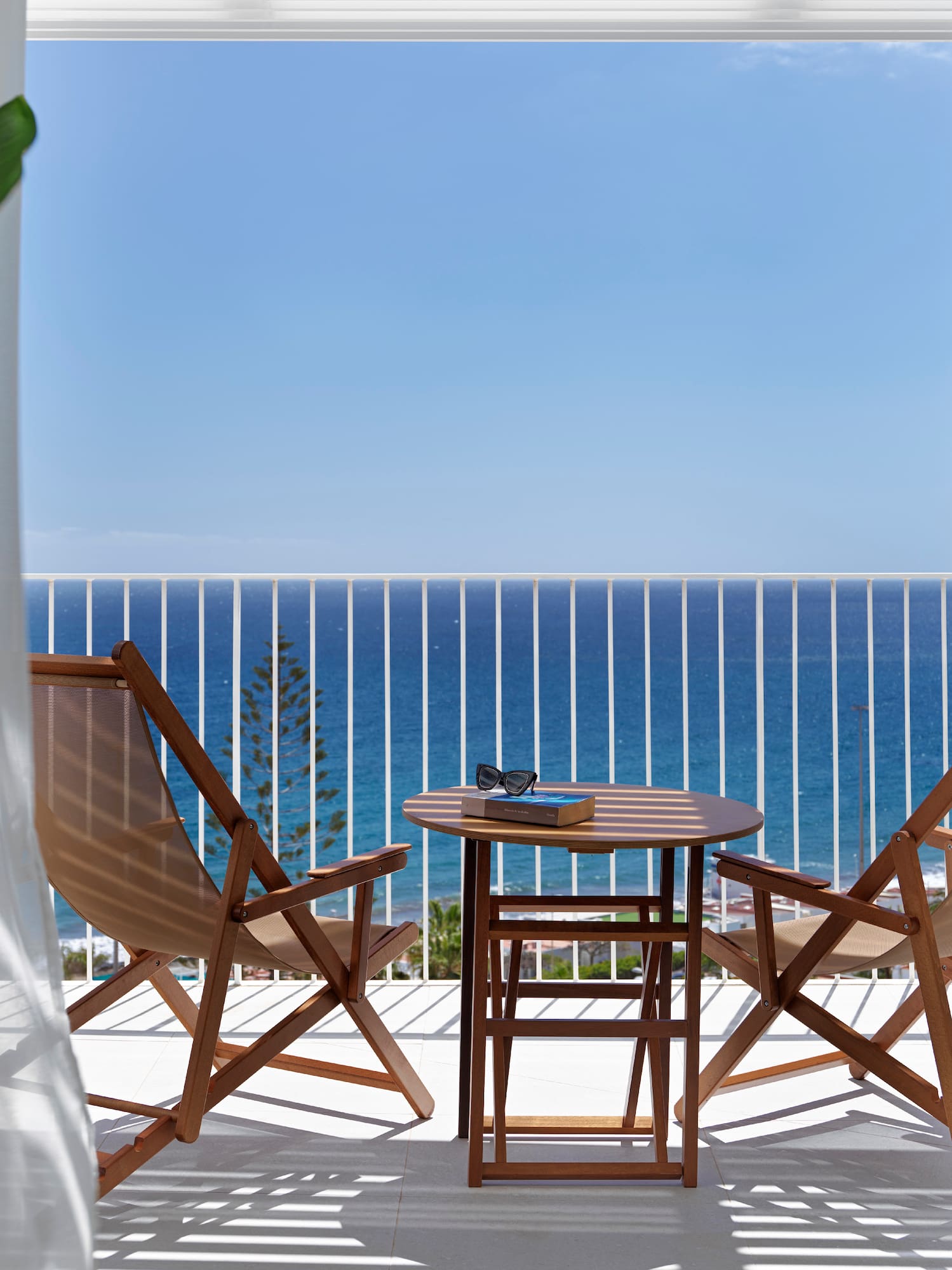 Ocean view balcony with wooden patio furniture, book, and sunglasses.