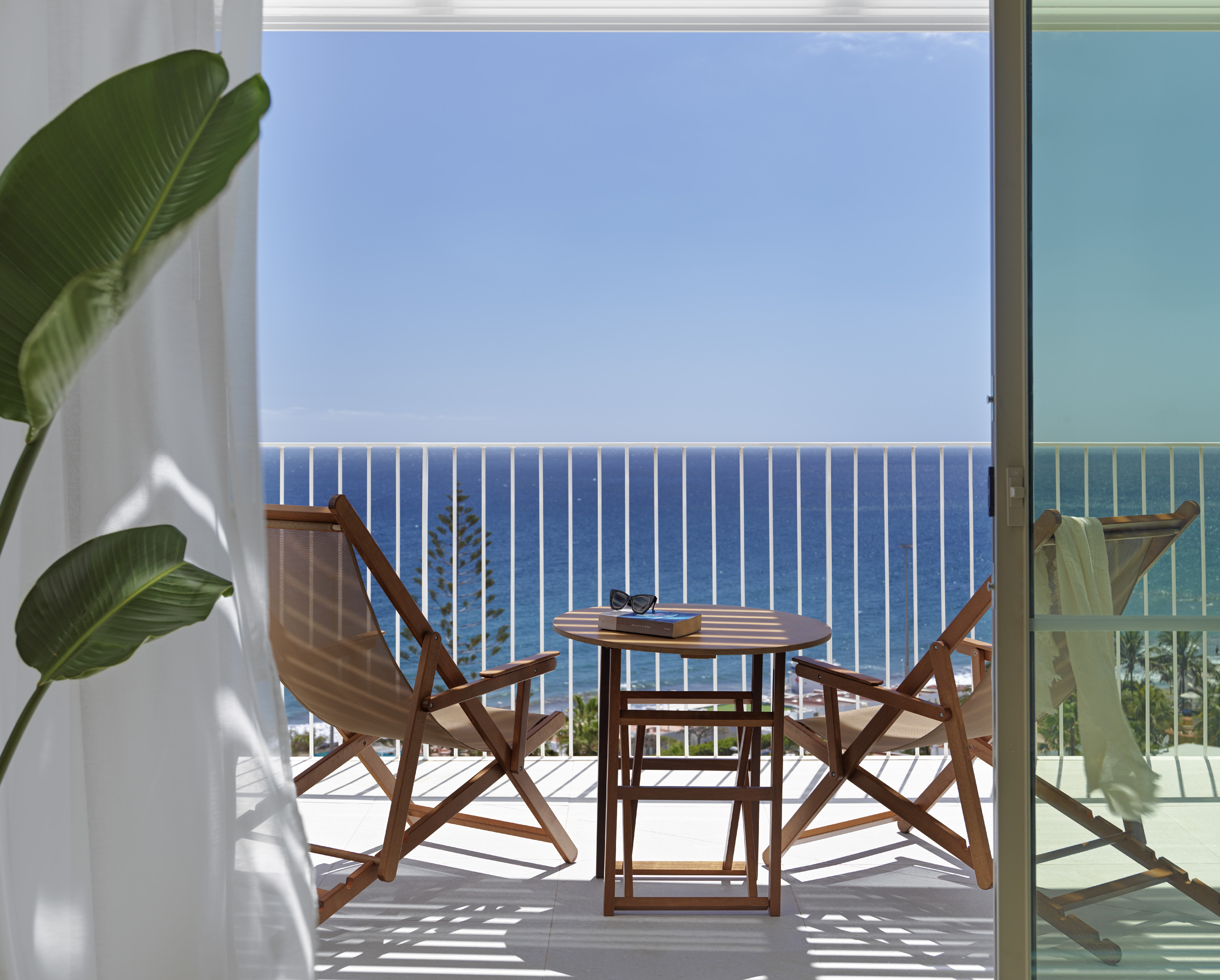 Ocean view balcony with wooden patio furniture, book, and sunglasses.