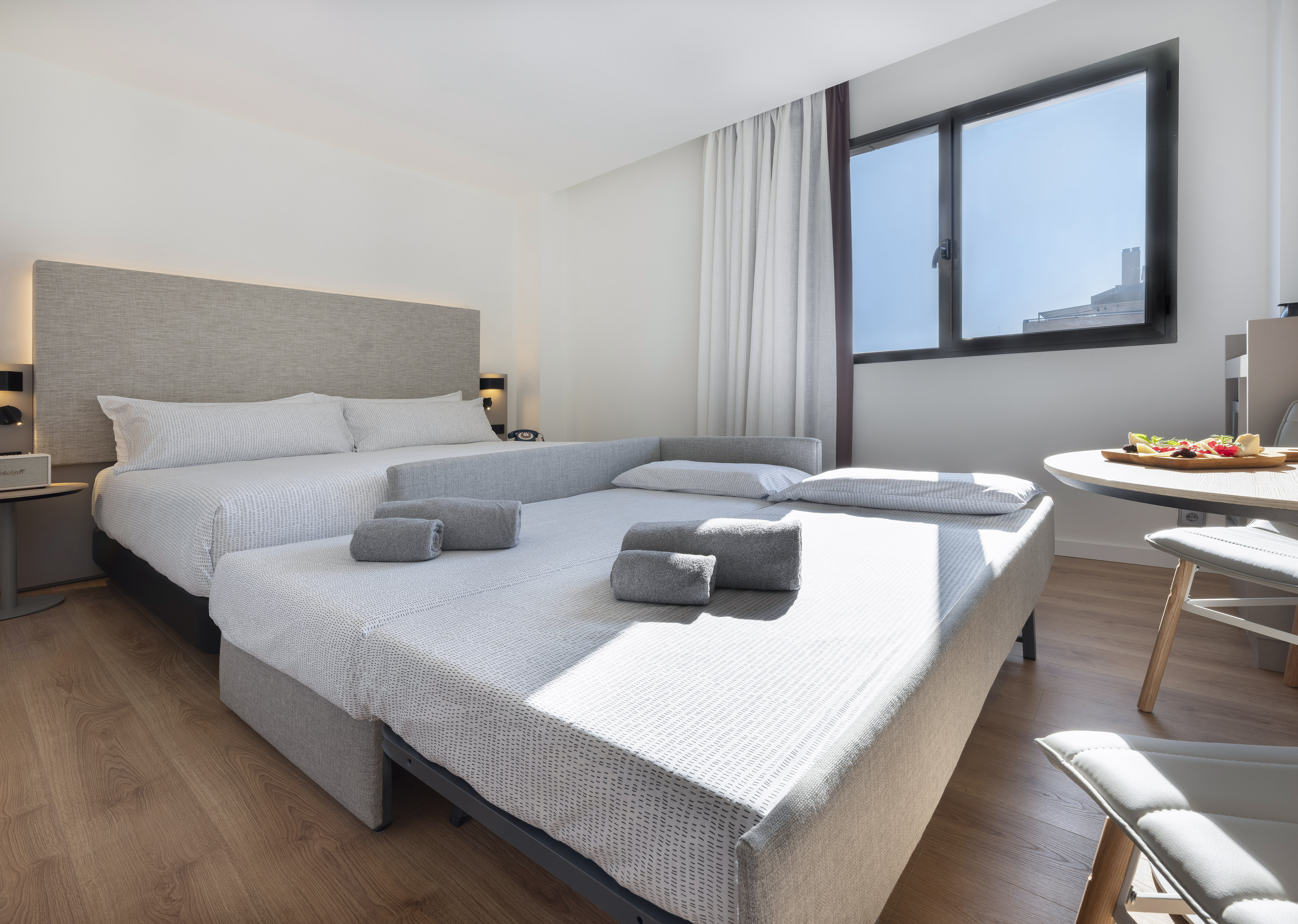 Bright hotel room with queen bed, pull-out sofa, wood floor, window.
