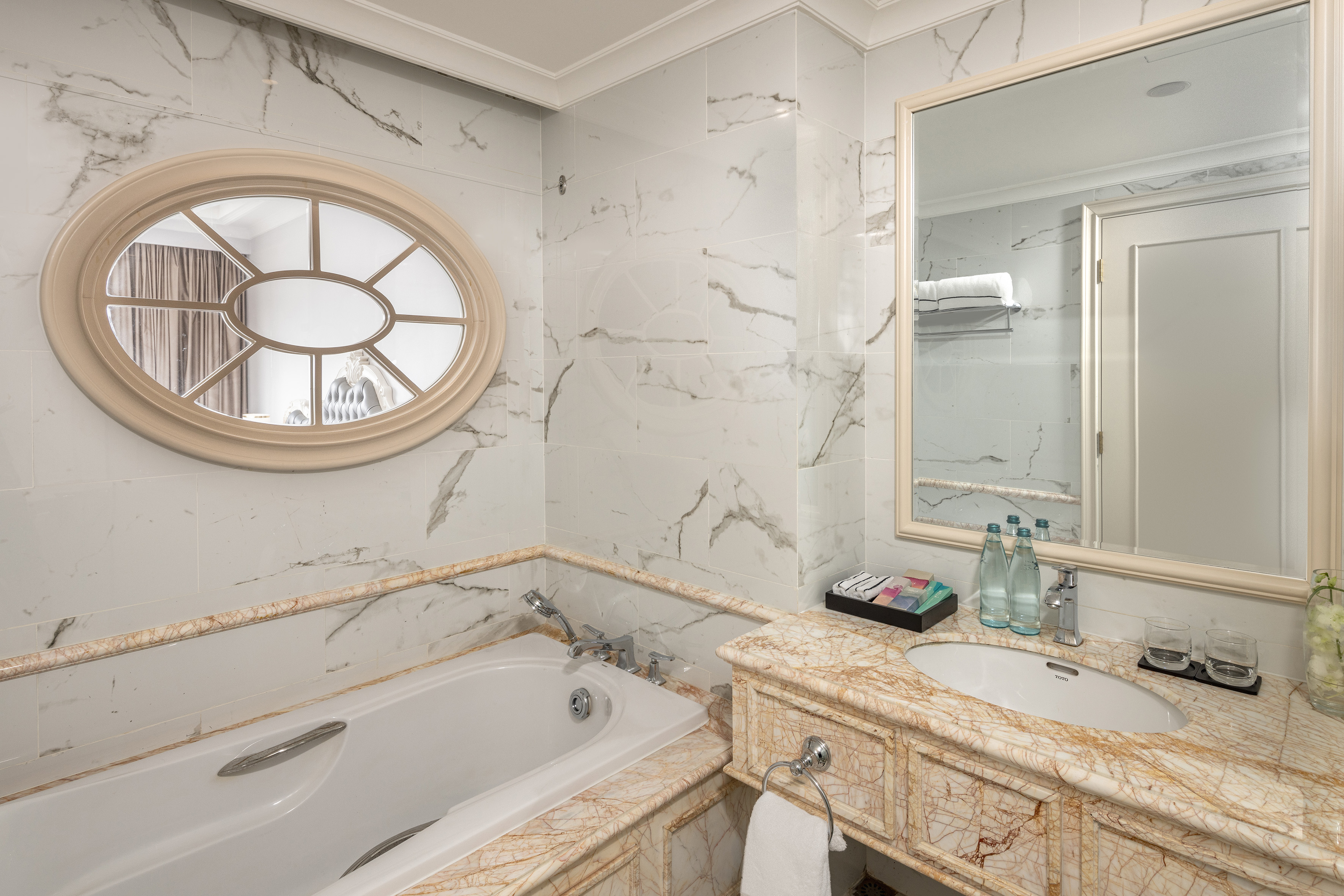Luxury marble bathroom with bathtub, oval mirror, and elegant vanity with sink.