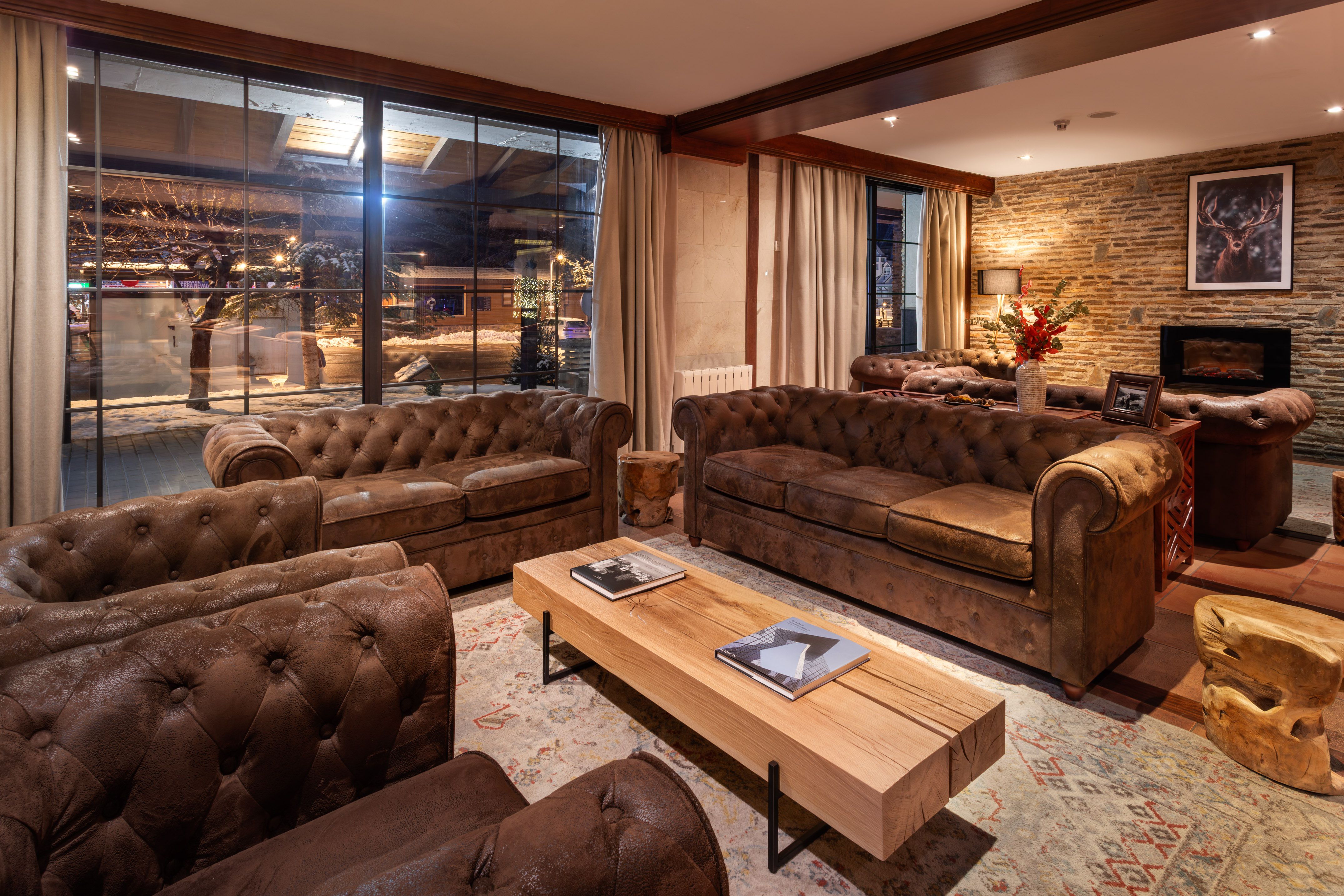 Cozy lodge lounge with leather sofas, fireplace, and snowy winter outside.