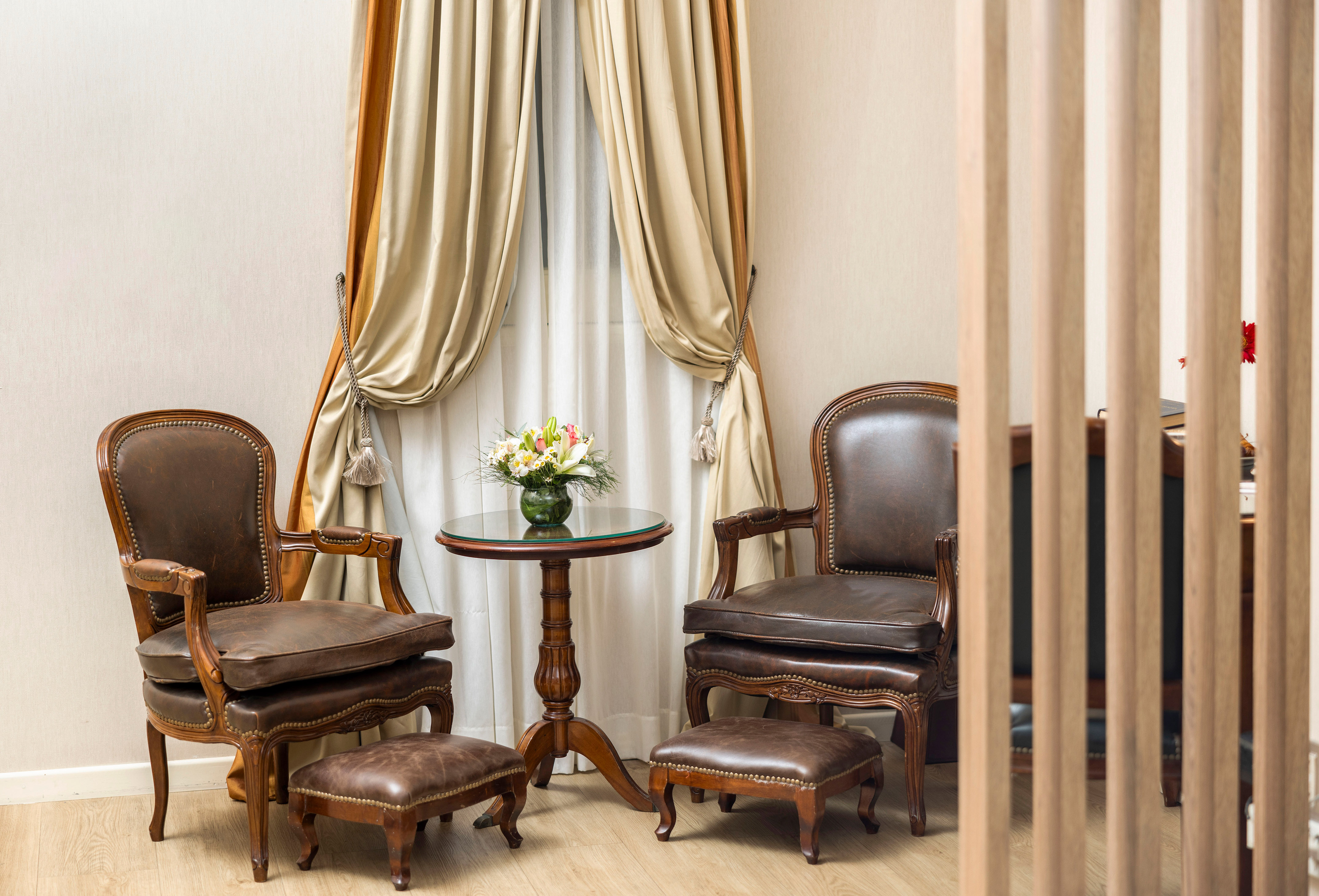 Elegant brown leather armchairs, footstools, and glass table with flowers.