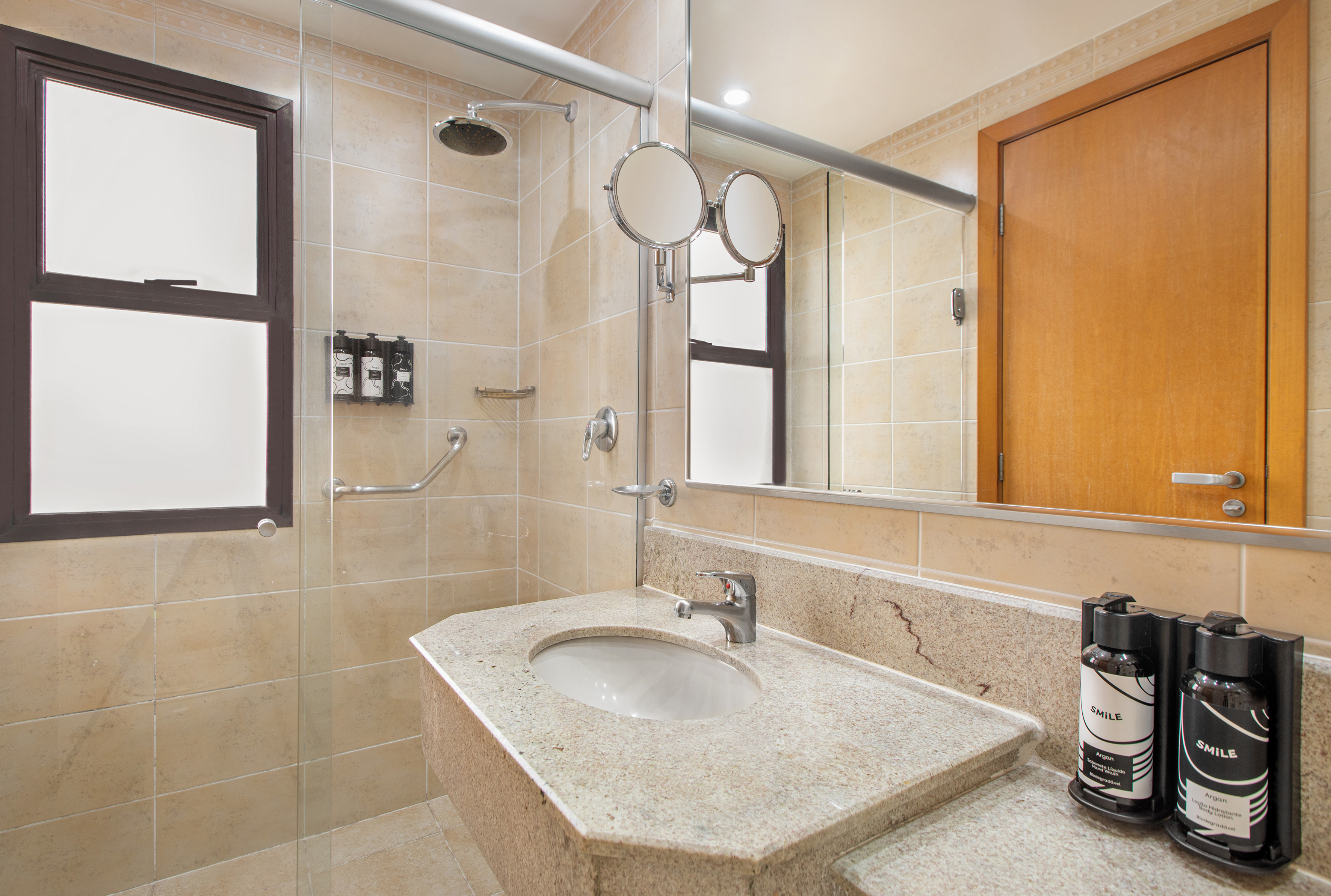 Modern accessible bathroom with beige tiles, shower, granite vanity, grab bar.