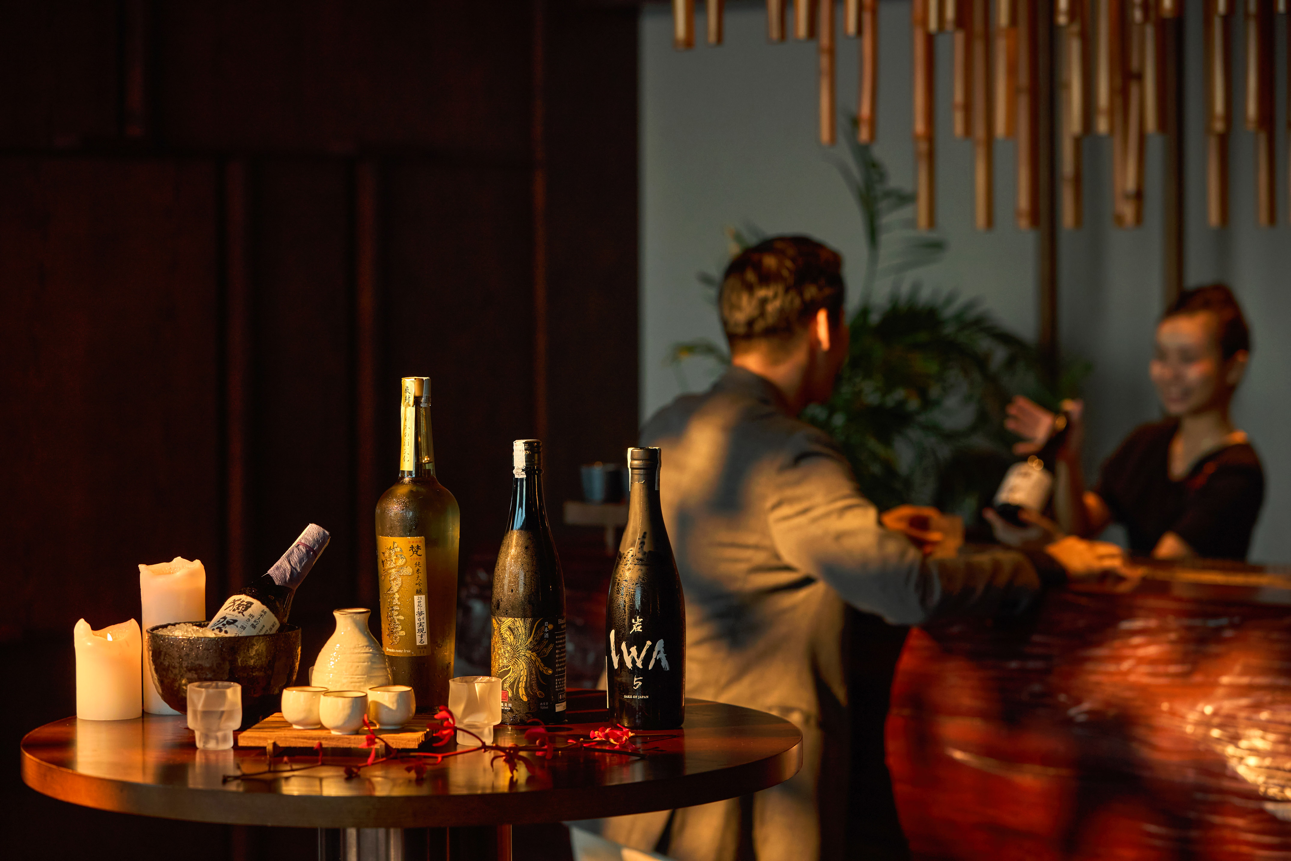 Premium IWA 5 sake bottles, tasting set, candles on a table in a bar.