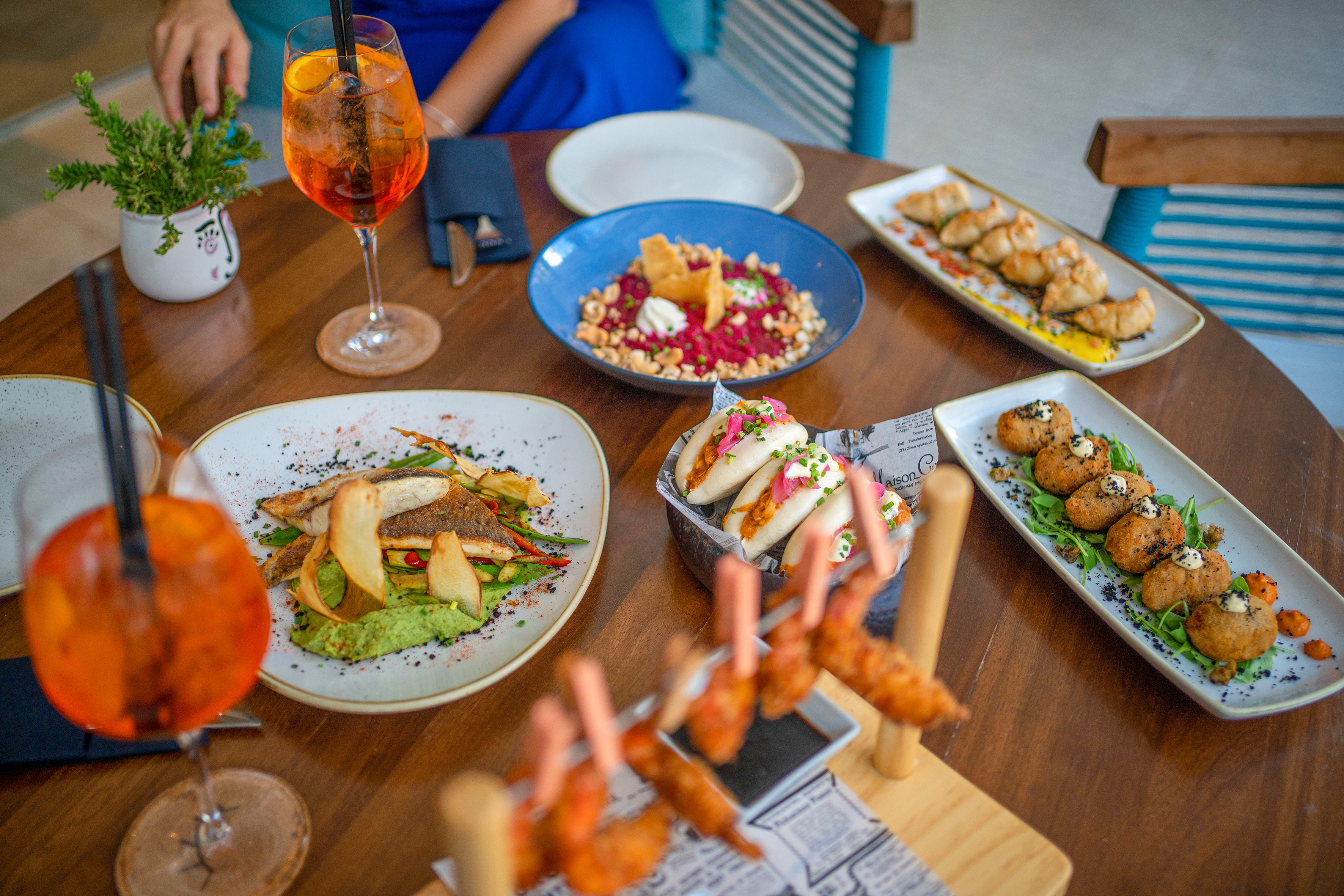 Restaurant table: cocktails, fish, bao buns, shrimp, croquettes, and dumplings.