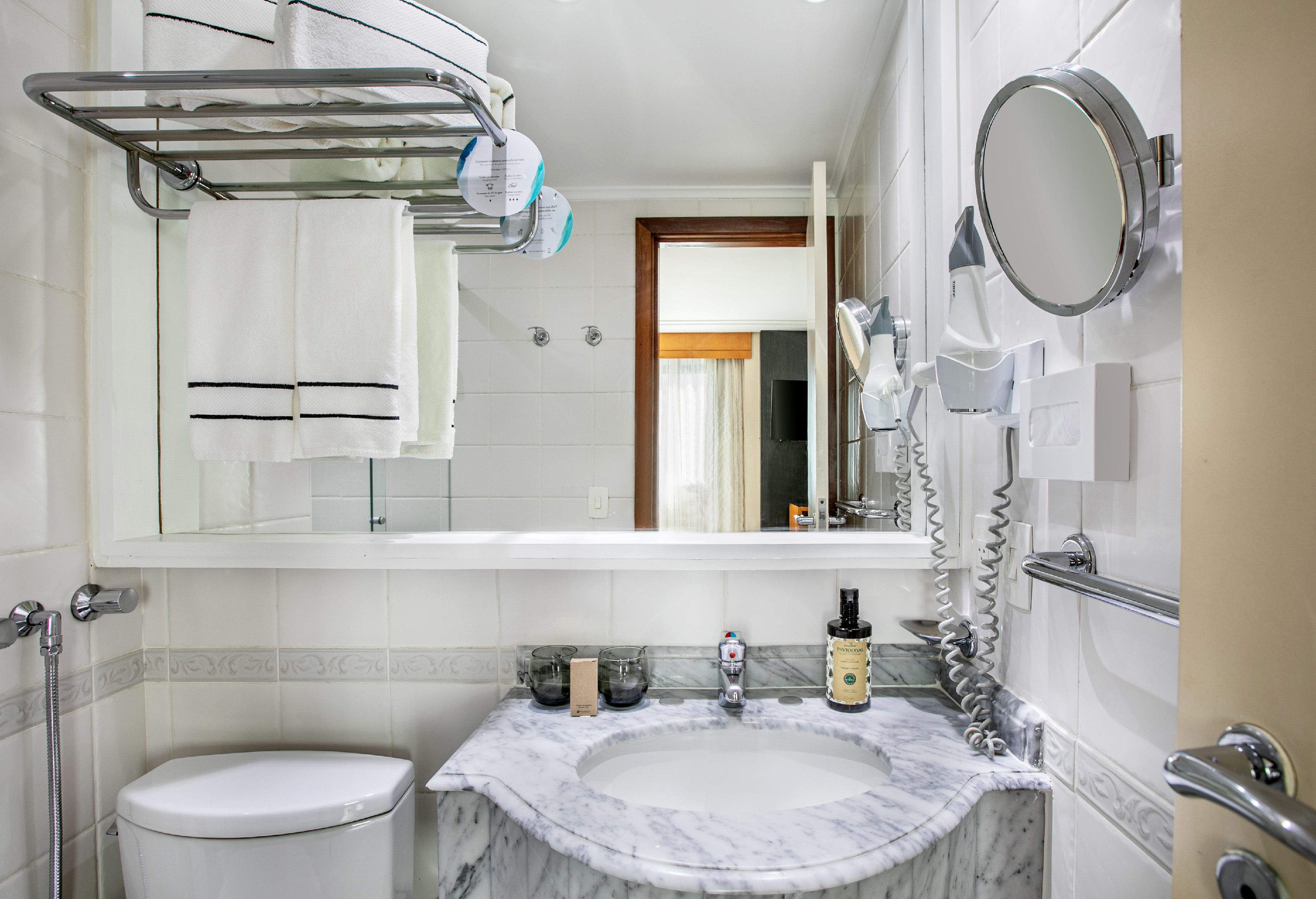 Hotel bathroom with marble sink, toilet, white towels, mirror, and hairdryer.