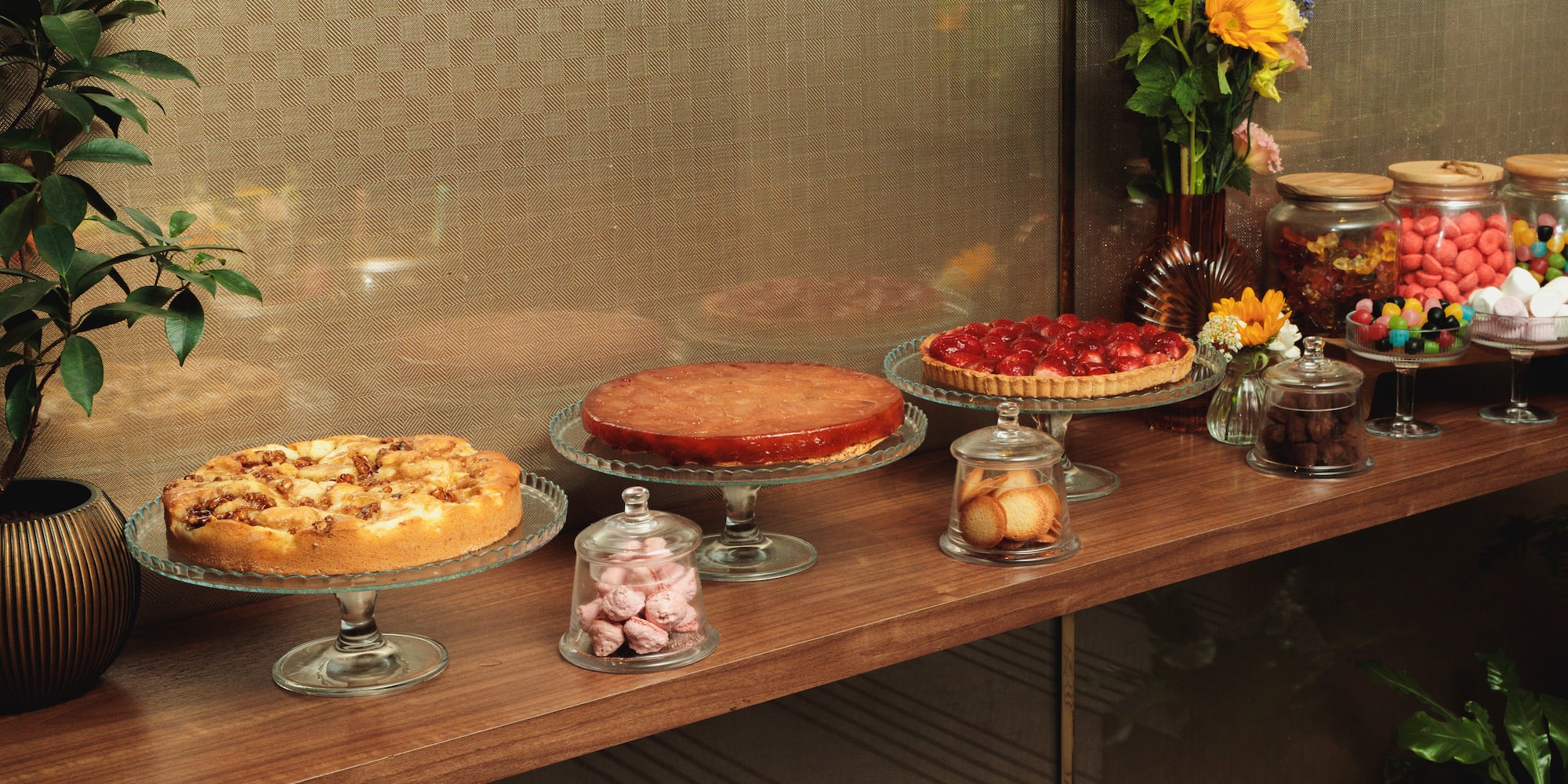A wooden dessert table displaying various cakes, tarts, and colorful candy jars.