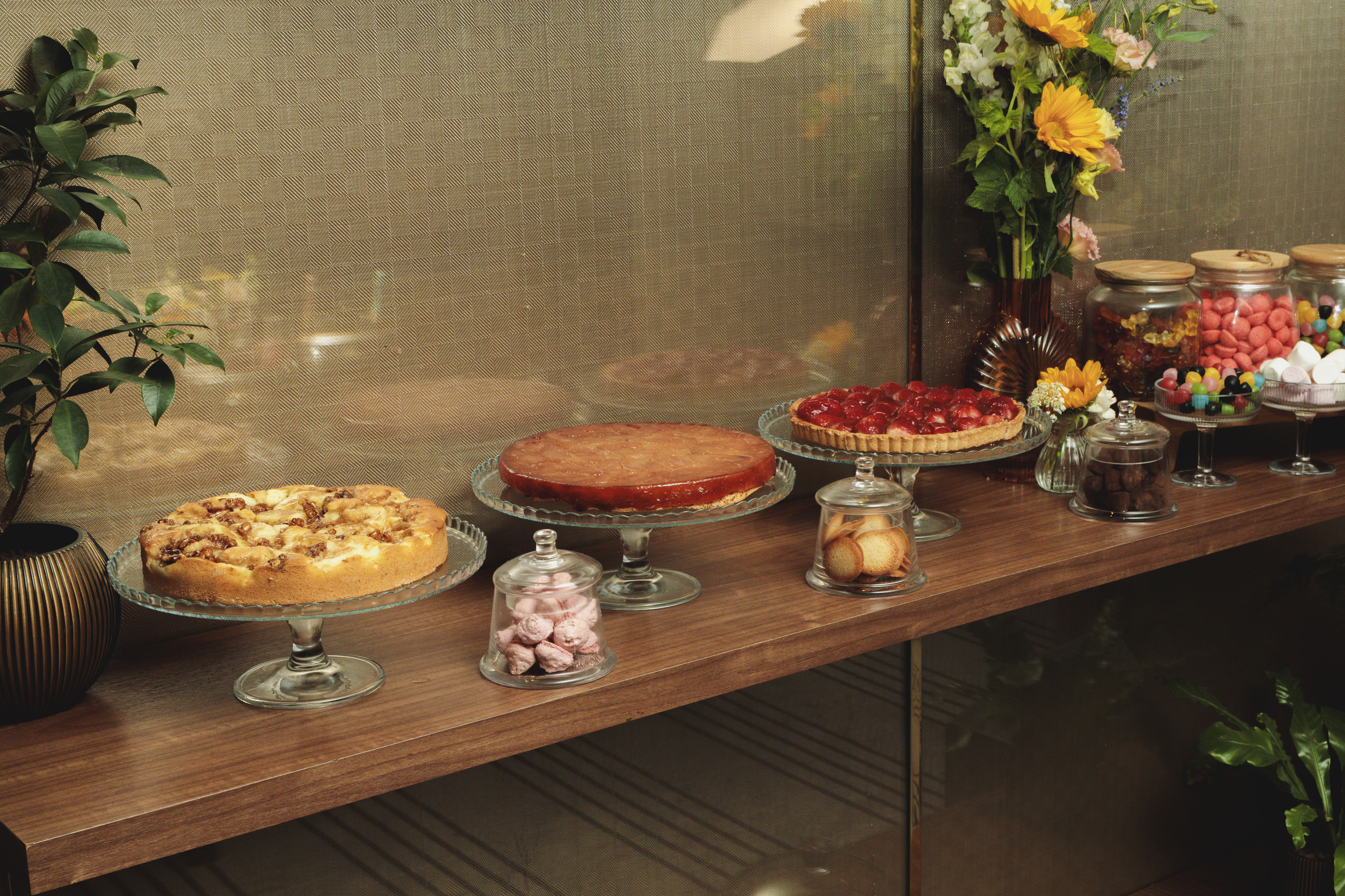 A wooden dessert table displaying various cakes, tarts, and colorful candy jars.